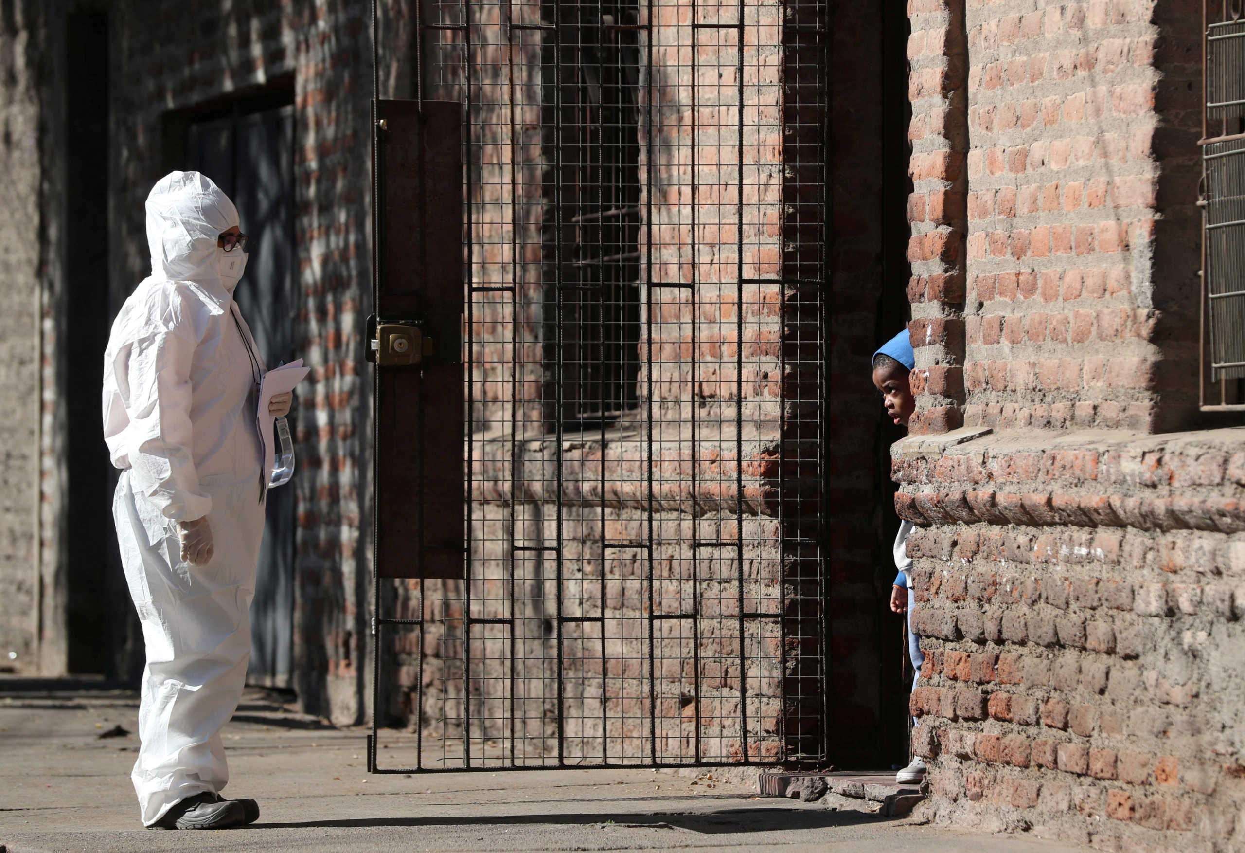 A woman wearing a protective suit talks to a child at a migrant neighbourhood during the start of a general quarantine to force down a surging rate of fresh coronavirus cases in the capital, amid the spread of the coronavirus disease (COVID-19) in Santiago, Chile May 16, 2020. REUTERS
