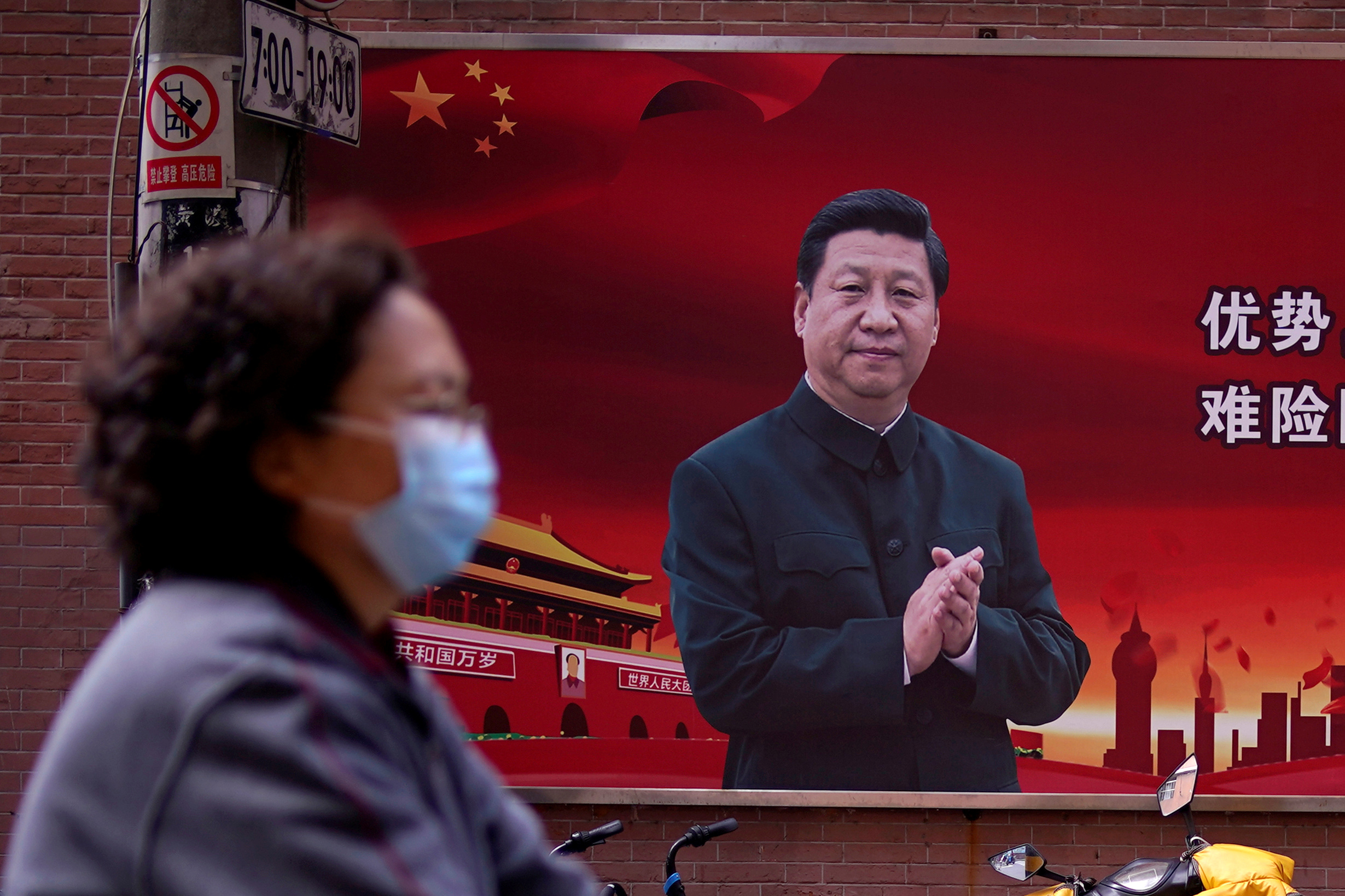 FILE PHOTO: A woman wearing a protective mask is seen past a portrait of Chinese President Xi Jinping on a street as the country is hit by an outbreak of the coronavirus, in Shanghai, China March 12, 2020. REUTERS