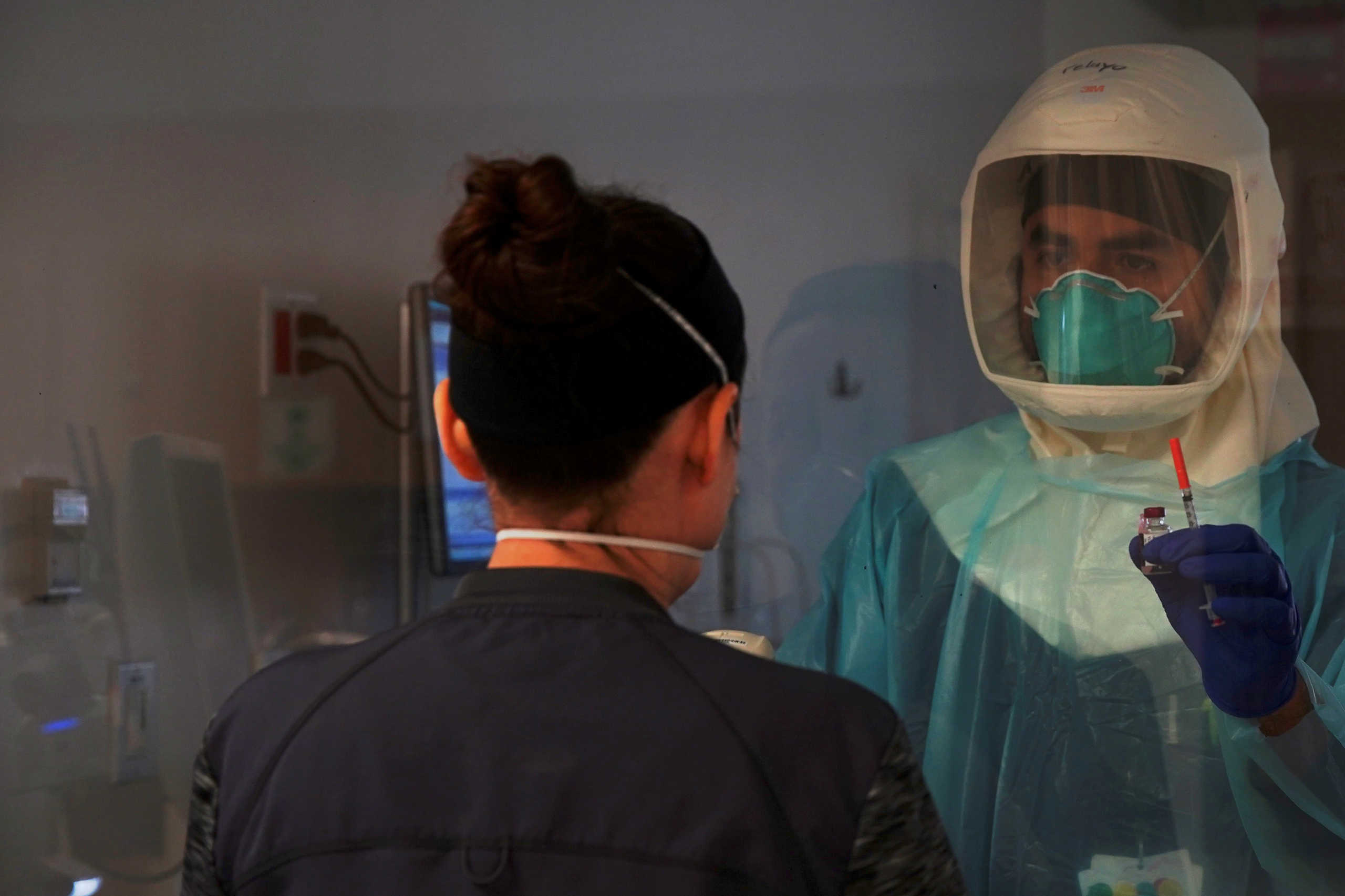 A healthcare worker wearing protective equipment and holding a syringe, while treating a patient with coronavirus disease (COVID-19), communicates to a registered nurse through a window from an isolated room at El Centro Regional Medical Center in El Centro, California, U.S., May 27, 2020. Picture taken May 27, 2020. REUTERS