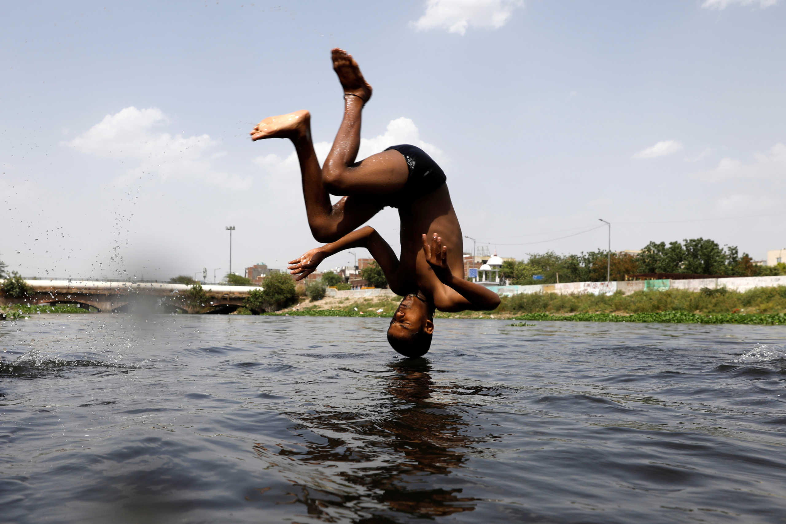 A boy jumps into a canal to cool off on a hot summer day in New Delhi, India, May 26, 2020. REUTERS