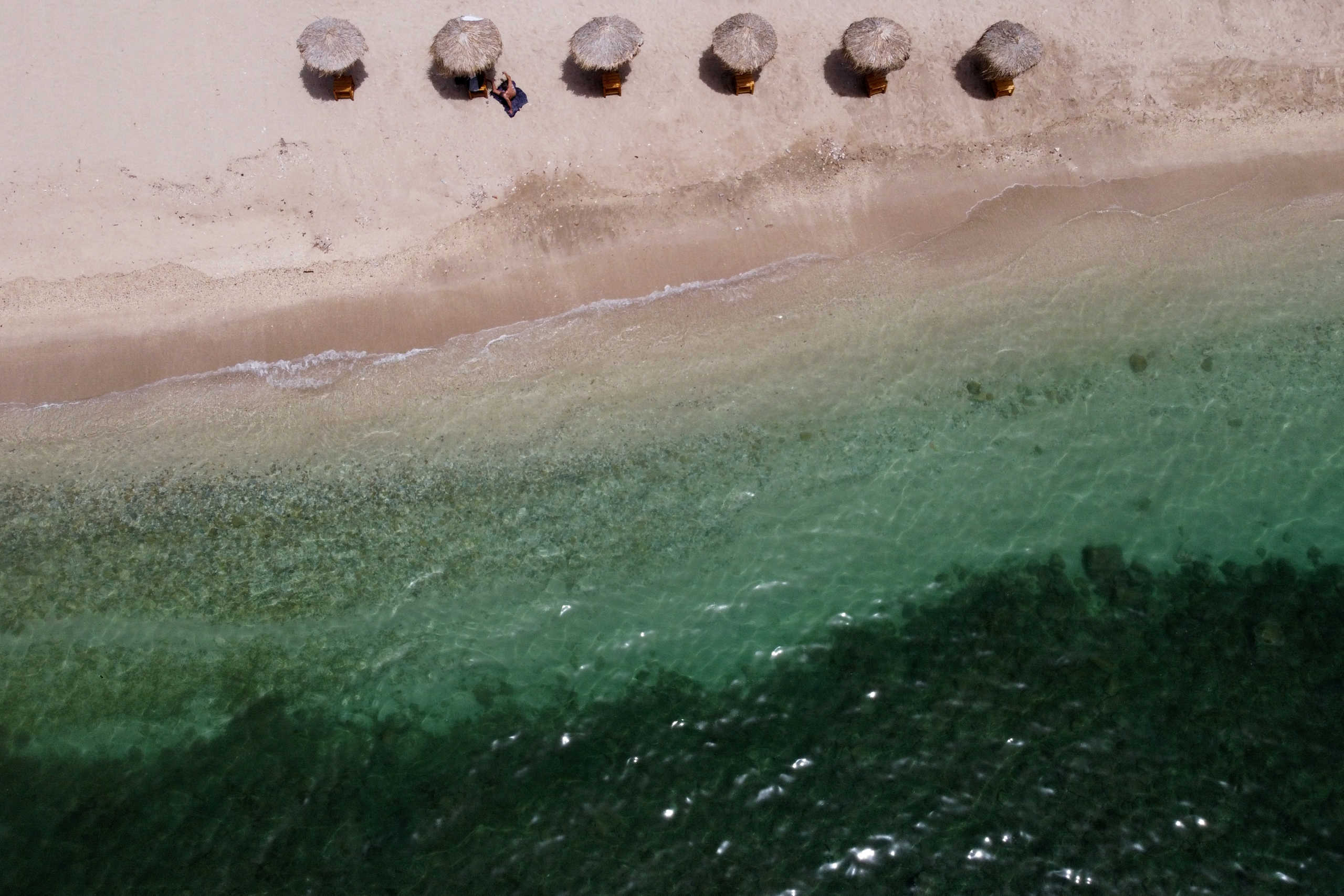 A man sunbathes on an empty beach, a day before the official opening of beaches to the public following the easing of measures against the spread of the coronavirus disease (COVID-19), in Athens, Greece, May 15, 2020. Picture taken with a drone. REUTERS