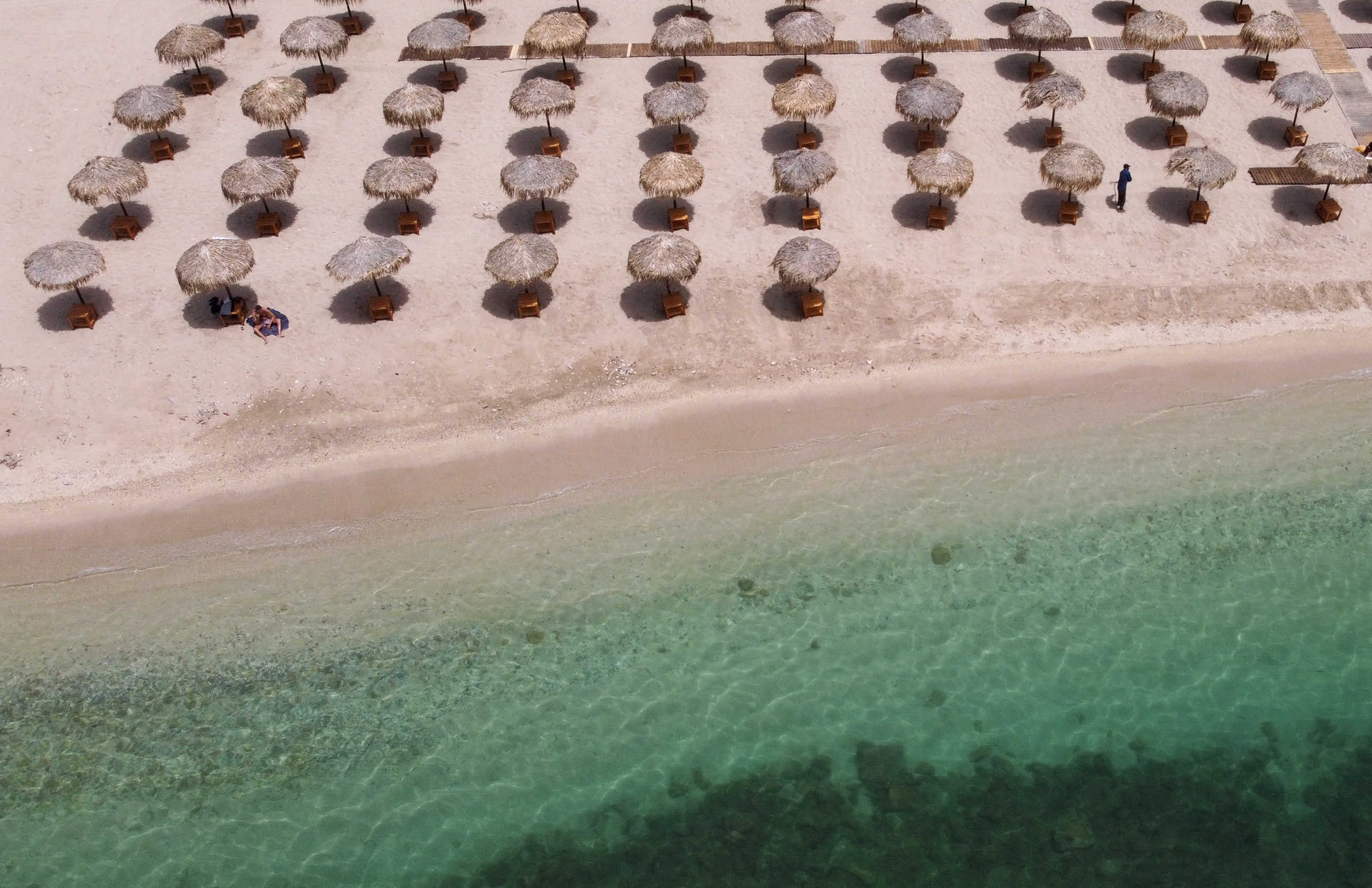 A man sunbathes as a worker rakes an empty beach, a day before the official opening of beaches to the public following the easing of measures against the spread of the coronavirus disease (COVID-19), in Athens, Greece, May 15, 2020. Picture taken with a drone. REUTERS