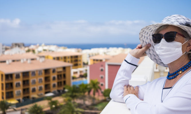 Elegantly dressed senior woman stays at home to avoid coronavirus infection, looking at the city from the balcony. Prevention and waiting for the end of the pandemic
