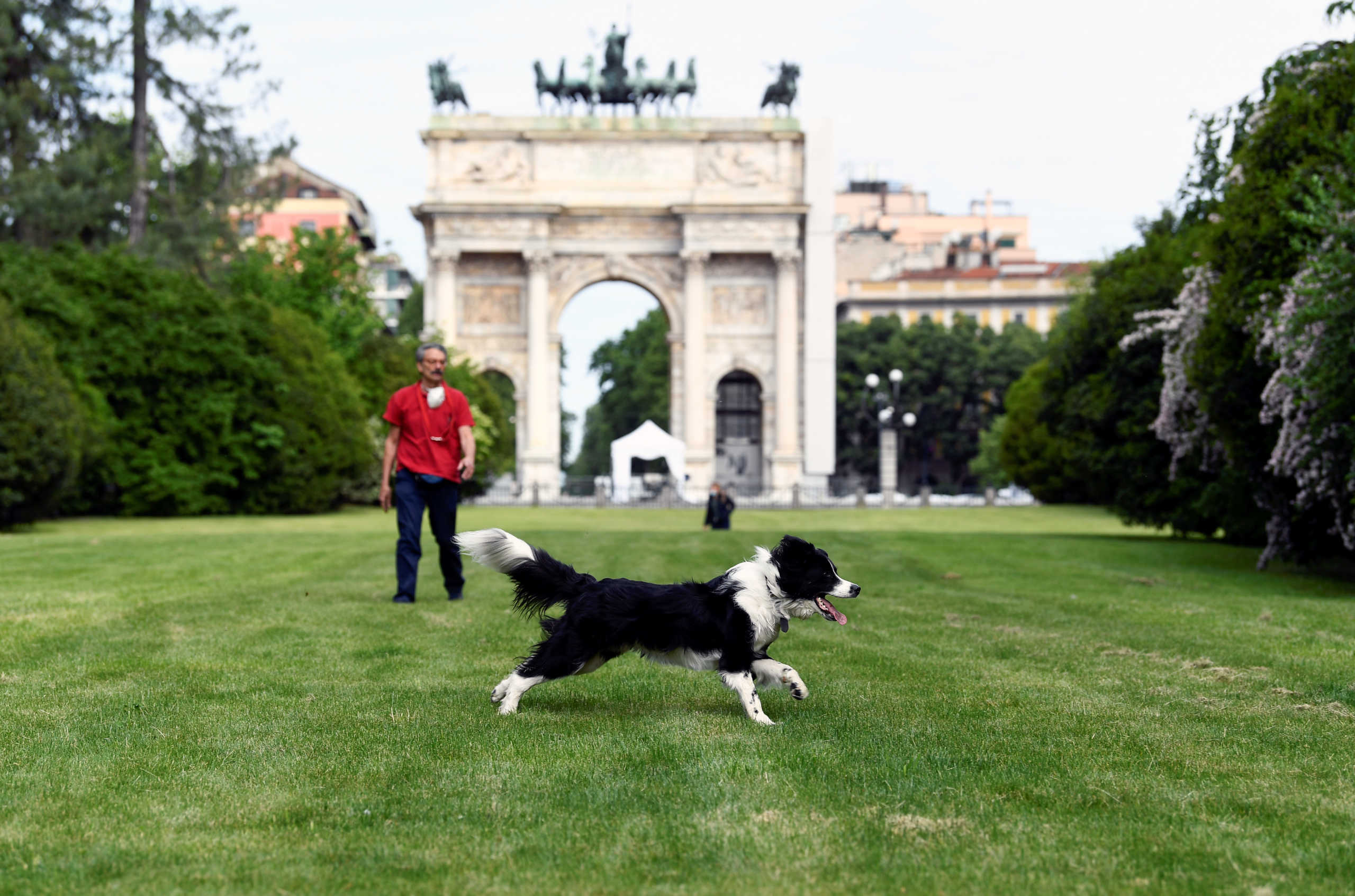 A man wearing a protective mask walks at the Sempione park next to a dog, after parks reopen as Italy begins a staged end to a nationwide lockdown due to a spread of the coronavirus disease (COVID-19), in Milan, Italy, May 4, 2020. REUTERS
