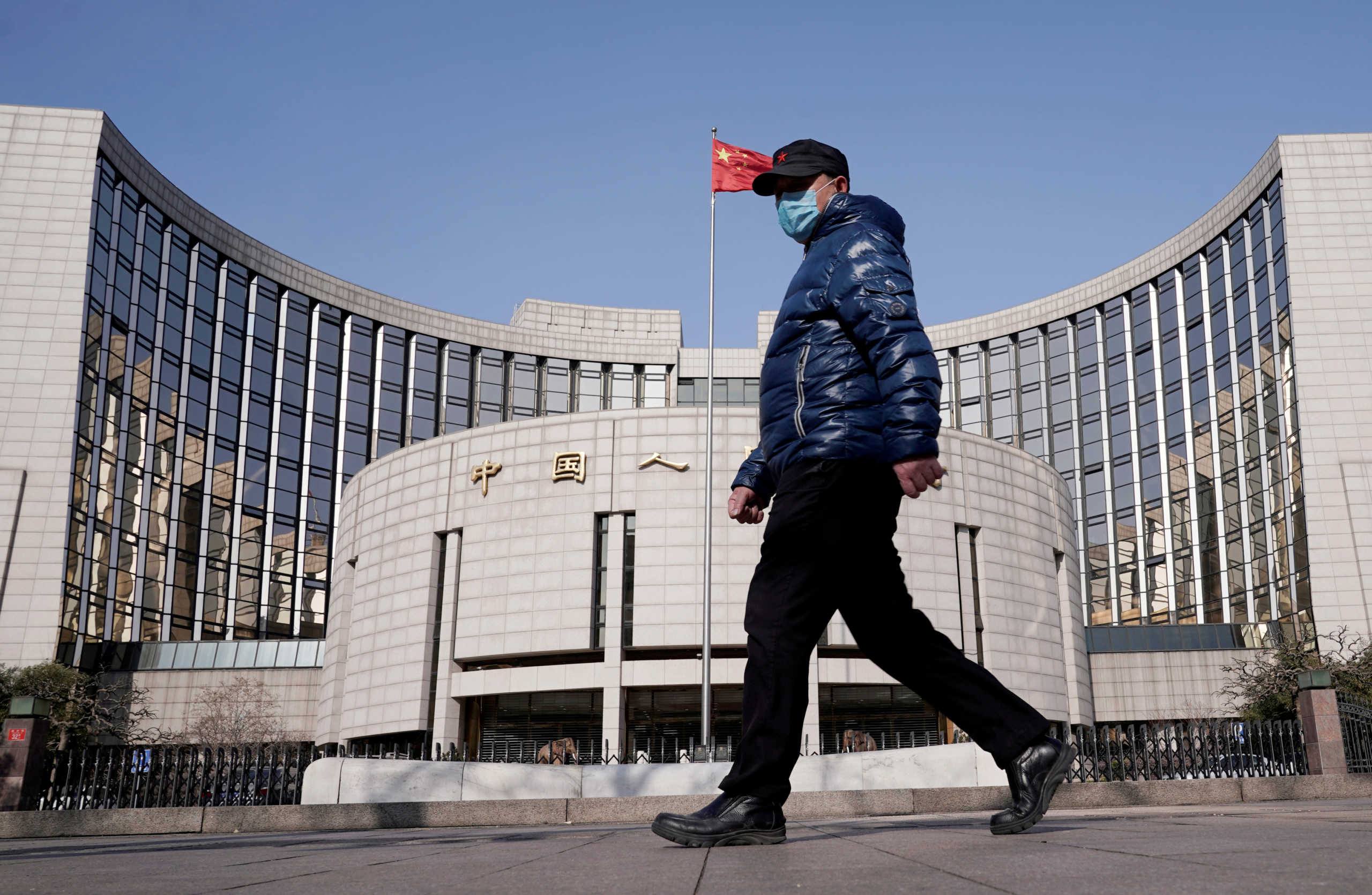 FILE PHOTO: A man wearing a mask walks past the headquarters of the People's Bank of China, the central bank, in Beijing, China, as the country is hit by an outbreak of the new coronavirus, February 3, 2020. REUTERS
