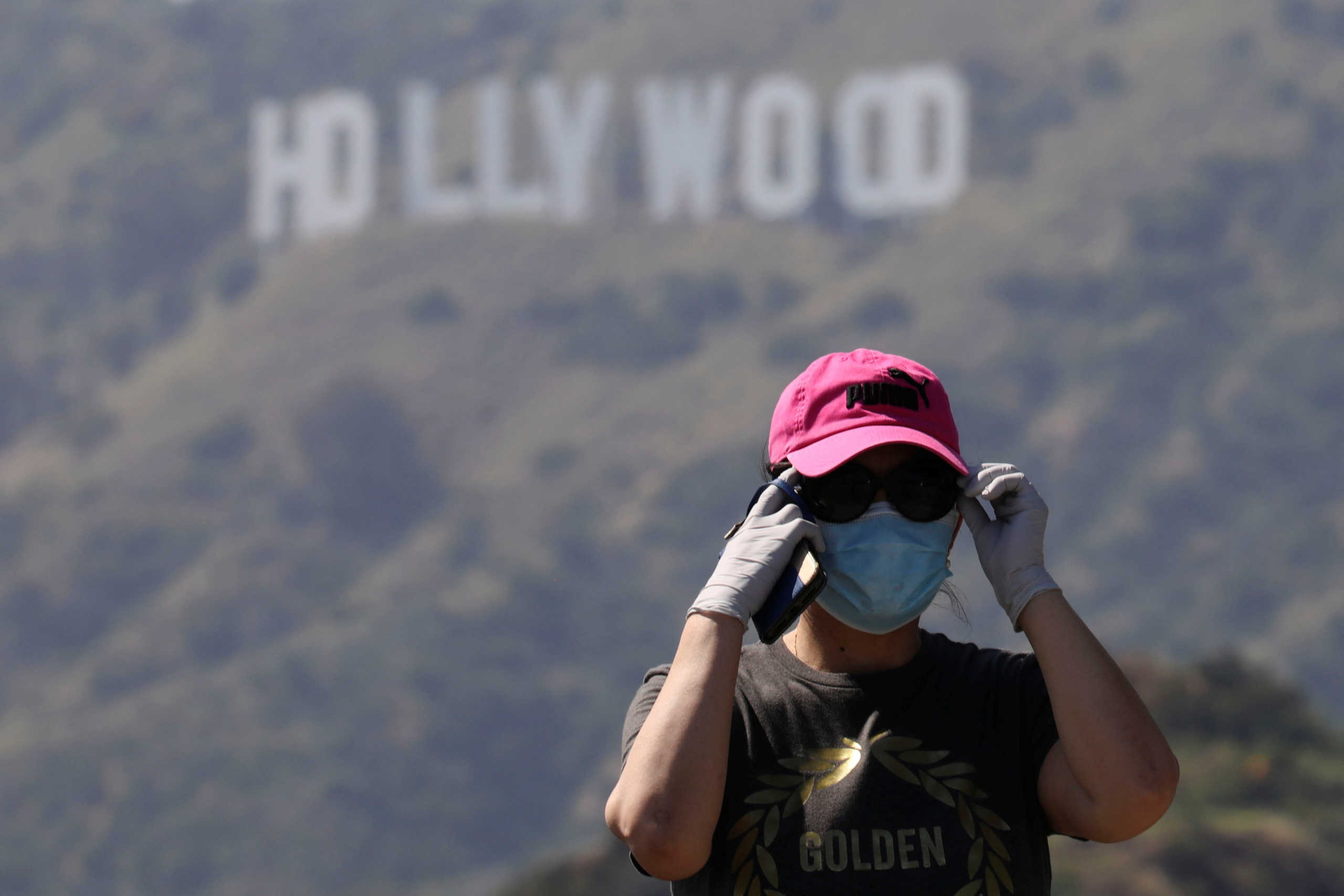 A person wearing a face mask and gloves adjusts glasses while taking photos of the Hollywood sign after a partial reopening of Los Angeles hiking trails during the outbreak of the coronavirus disease (COVID-19) at Griffith Park in Los Angeles, California, U.S., May 9, 2020. REUTERS