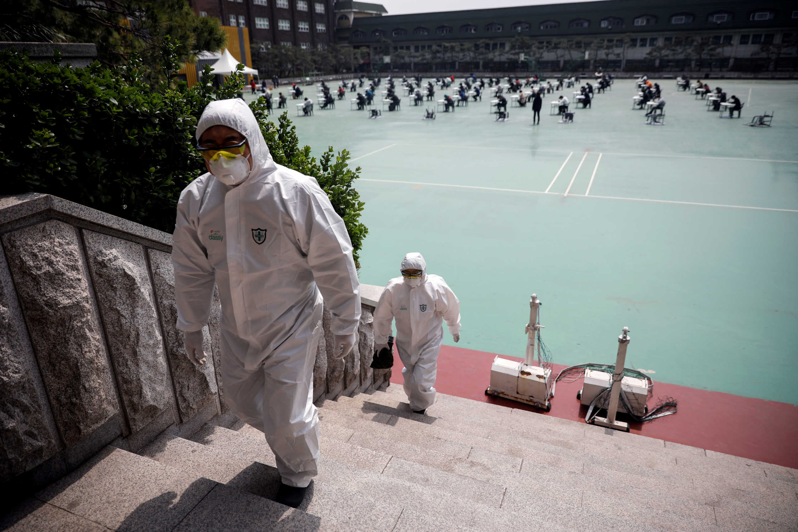FILE PHOTO: People in personal protective equipment walk up a flight of stairs as South Korean job seekers (background) attend an exam conducted outdoors amid social distancing measures to avoid the spread of the coronavirus disease (COVID-19), in Seoul, South Korea, April 25, 2020. REUTERS