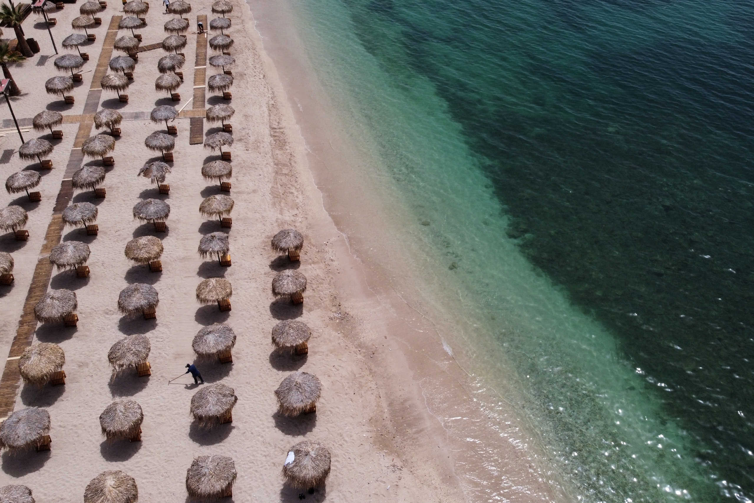 A worker rakes an empty beach, a day before the official opening of beaches to the public following the easing of measures against the spread of the coronavirus disease (COVID-19), in Athens, Greece, May 15, 2020. Picture taken with a drone. REUTERS
