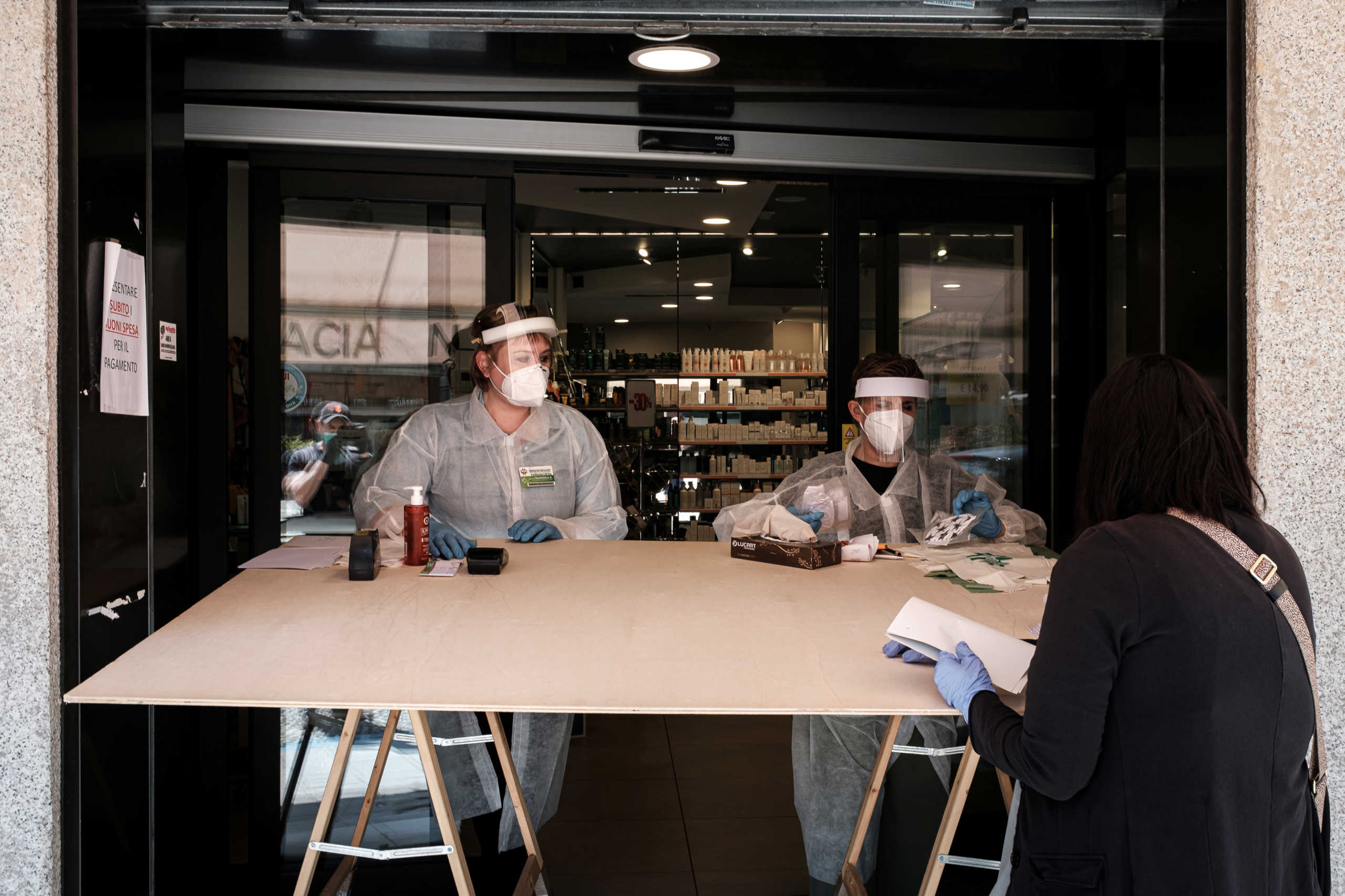 Life in Italy's original 'red zones': Chemists wearing full protective gears serve a customer from behind a large table outside their shop as a way of social distancing in Codogno, the small northern town where Italy's first patient was diagnosed with the coronavirus disease (COVID-19) on February 21, as the country begins a staged end to a nationwide lockdown, in this picture taken by schoolteacher Marzio Toniolo, May 4, 2020. Many owners in the town are not allowing customers inside their shops, and instead taking orders from outside to try and avoid contagion. Codogno residents had been on lockdown for over 10 weeks, as they were part of a small cluster of northern towns where cases and deaths immediately surged after the first patient was diagnosed. Picture taken May 4, 2020. Marzio Toniolo via REUTERS THIS IMAGE HAS BEEN SUPPLIED BY A THIRD PARTY. MANDATORY CREDIT