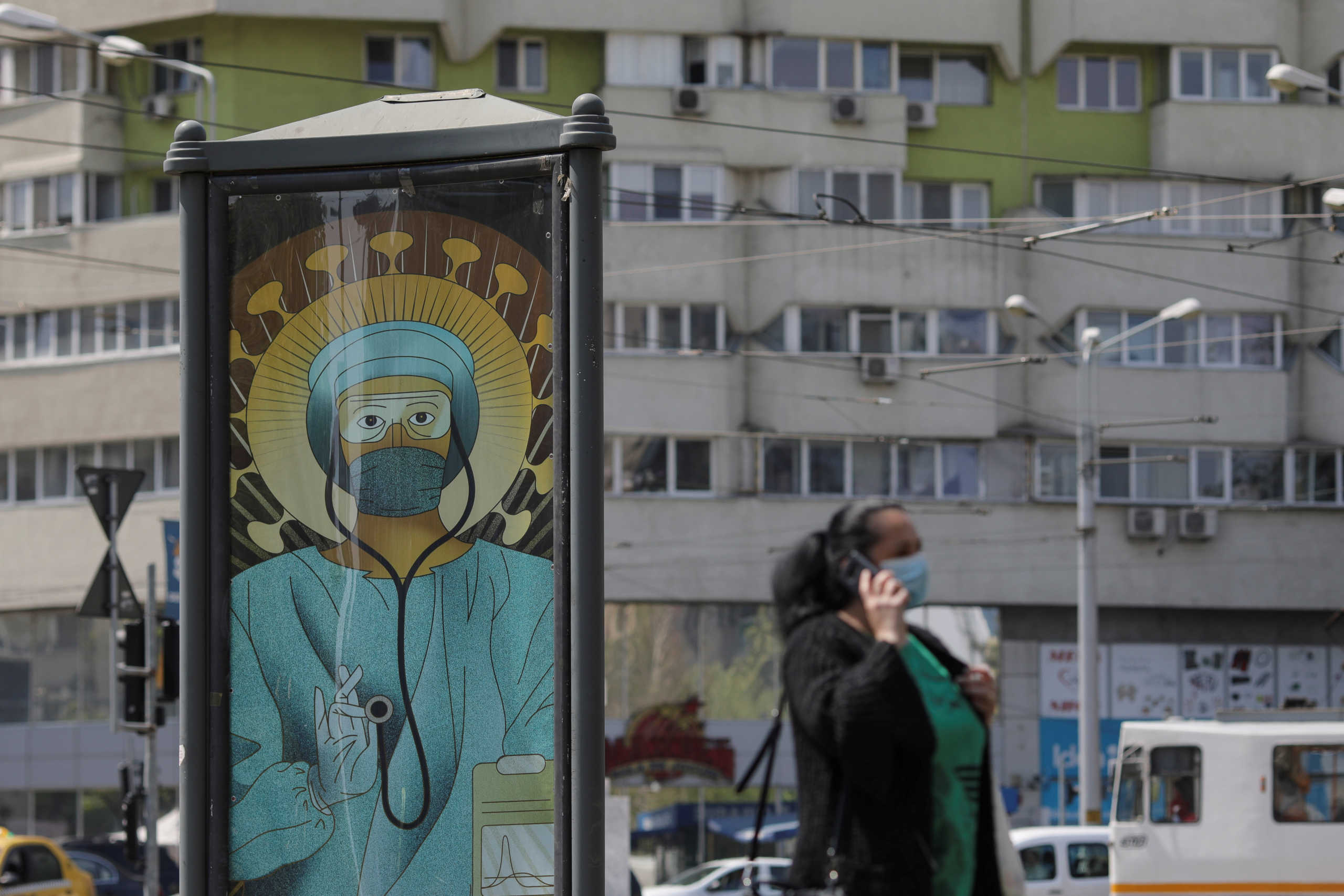 A woman wearing a medical mask passes by an outdoor poster that shows a medic depicted in a similar manner as Jesus Christ would be portrayed by Christian Orthodox religious paintings, in Bucharest, Romania, April 29, 2020. The poster, created by Romanian illustrator Wanda Hutira, is part of a "Thank you doctors" campaign. Inquam Photos
