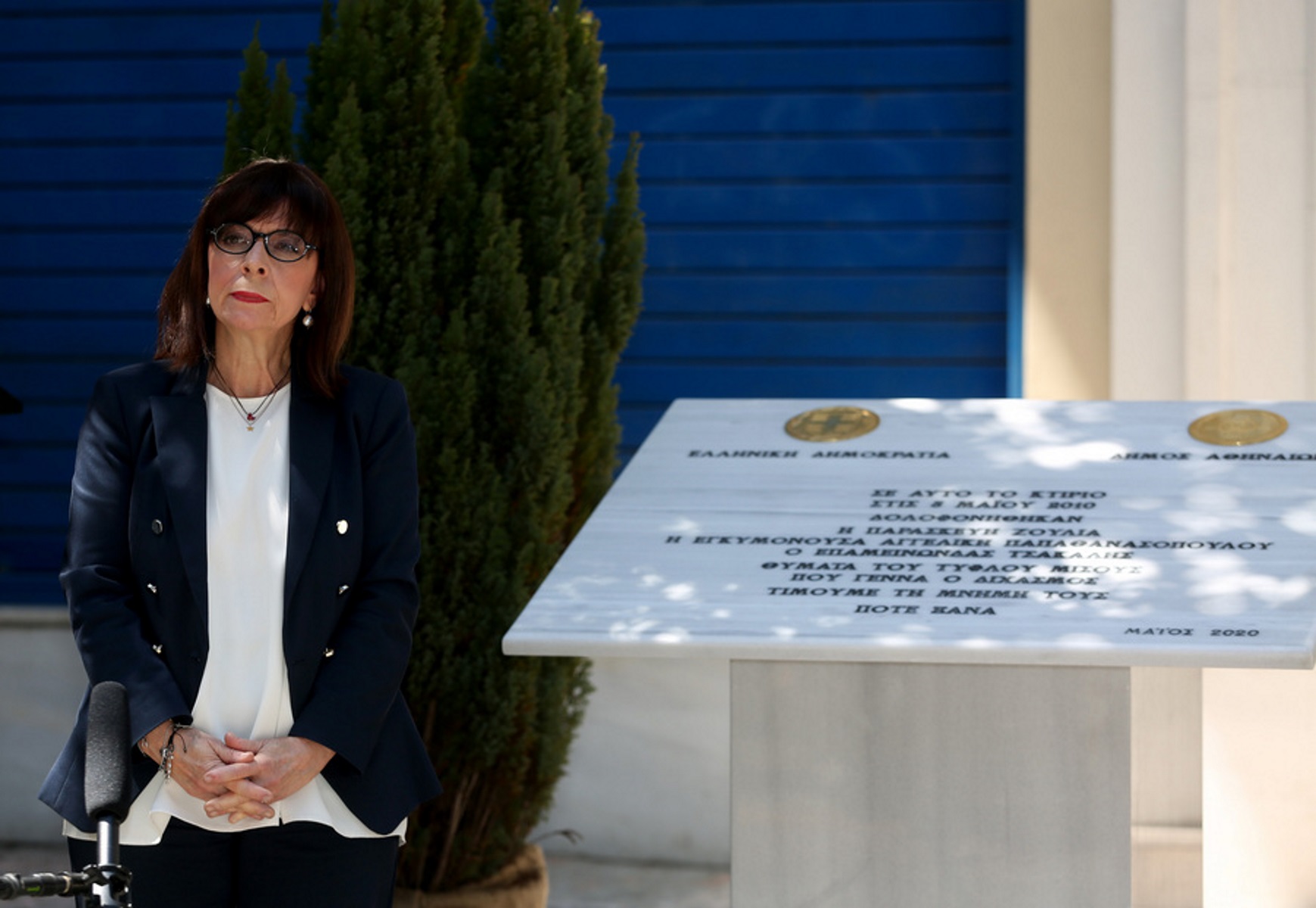Η Πρόεδρος της Δημοκρατίας Κατερίνα Σακελλαροπούλου δίπλα από την πλακέτα κατά τη διάρκεια της τελετής των αποκαλυπτηρίων της, στο χώρο όπου δολοφονήθηκαν οι τρεις εργαζόμενοι της Marfin, στην οδό Σταδίου, το Σάββατο 9 Μαΐου 2020. Πέρασαν 10 χρόνια και 4 μέρες από τα θλιβερά γεγονότα στην τράπεζα Marfin - Εγνατία, στην οδό Σταδίου, η τραγωδία έγινε στις 5 Μαΐου του 2010 όπου κατά τη διάρκεια διαδηλώσεων κατά των οικονομικών μέτρων για την υπογραφή της δανειακής σύμβασης ομάδα αγνώστων, έριξαν βόμβες μολότοφ στην τράπεζα την ώρα που βρίσκονταν μέσα σε αυτήν περίπου 25-30 εργαζόμενοι. Οι περισσότεροι κατόρθωσαν να διαφύγουν, πέντε άτομα διέσωσε η Πυροσβεστική, τρεις όμως άνθρωποι πέθαναν από ασφυξία λόγω των τοξικών αναθυμιάσεων και του πυκνού καπνού. Η ταυτότητα των αυτουργών της επίθεσης δεν έχει επιβεβαιωθεί μέχρι και σήμερα. Στη μνήμη των θυμάτων της τραγωδίας, της Αγγελικής Παπαθανασοπούλου (32 ετών-έγκυος 4 μηνών), του Επαμεινώνδα Τσάκαλη (36 ετών) και της Παρασκευής Ζούλια (35 ετών) έγινε ο εντοιχισμός πλακέτας, στο χώρο όπου δολοφονήθηκαν οι εργαζόμενοι της Marfin, με πρωτοβουλία του πρωθυπουργού Κυριάκου Μητσοτάκη και παρουσία της Προέδρου της Δημοκρατίας Κατερίνας Σακελλαροπούλου και πολιτικών αρχηγών από κόμματα της αντιπολίτευσης. Νωρίτερα, στο σημείο κατέθεσαν στεφάνια ο πρόεδρος του ΣΥΡΙΖΑ Αλέξης Τσίπρας και ο γγ του ΚΚΕ Δημήτρης Κουτσούμπας. ΑΠΕ-ΜΠΕ