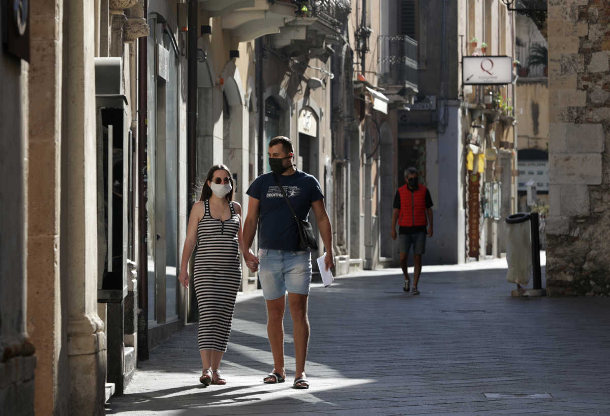 A couple wearing face masks is holding hands in a deserted street, as Italy begins to ease some of the restrictions of the coronavirus disease (COVID-19) lockdown, in Taormina, Italy, May 12, 2020. REUTERS
