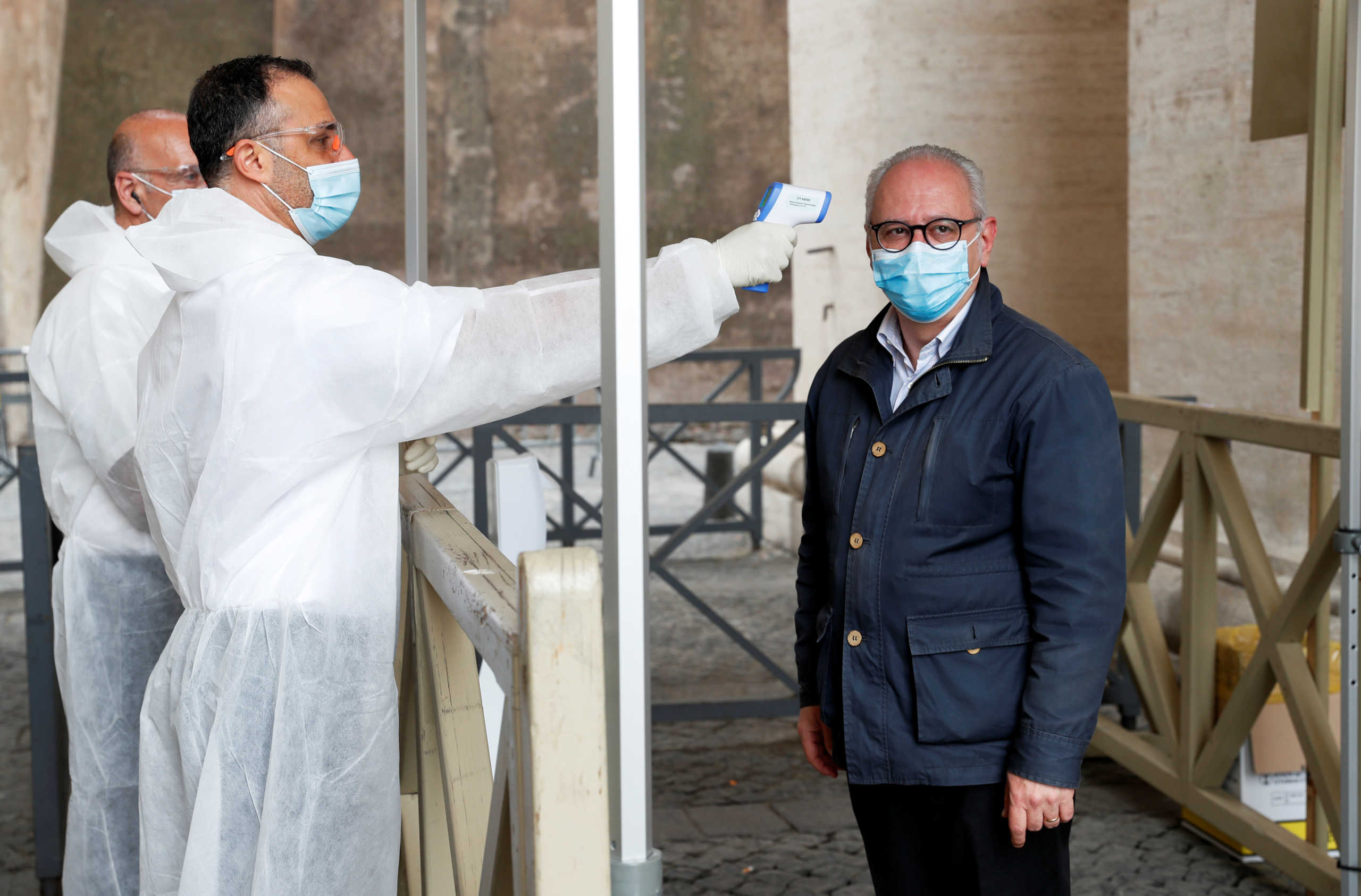 A worker in a protective suit measures the temperature of a man as Italy allows mass to resume after months of closure, during the coronavirus disease (COVID-19) outbreak, at the Vatican, May 18, 2020. REUTERS