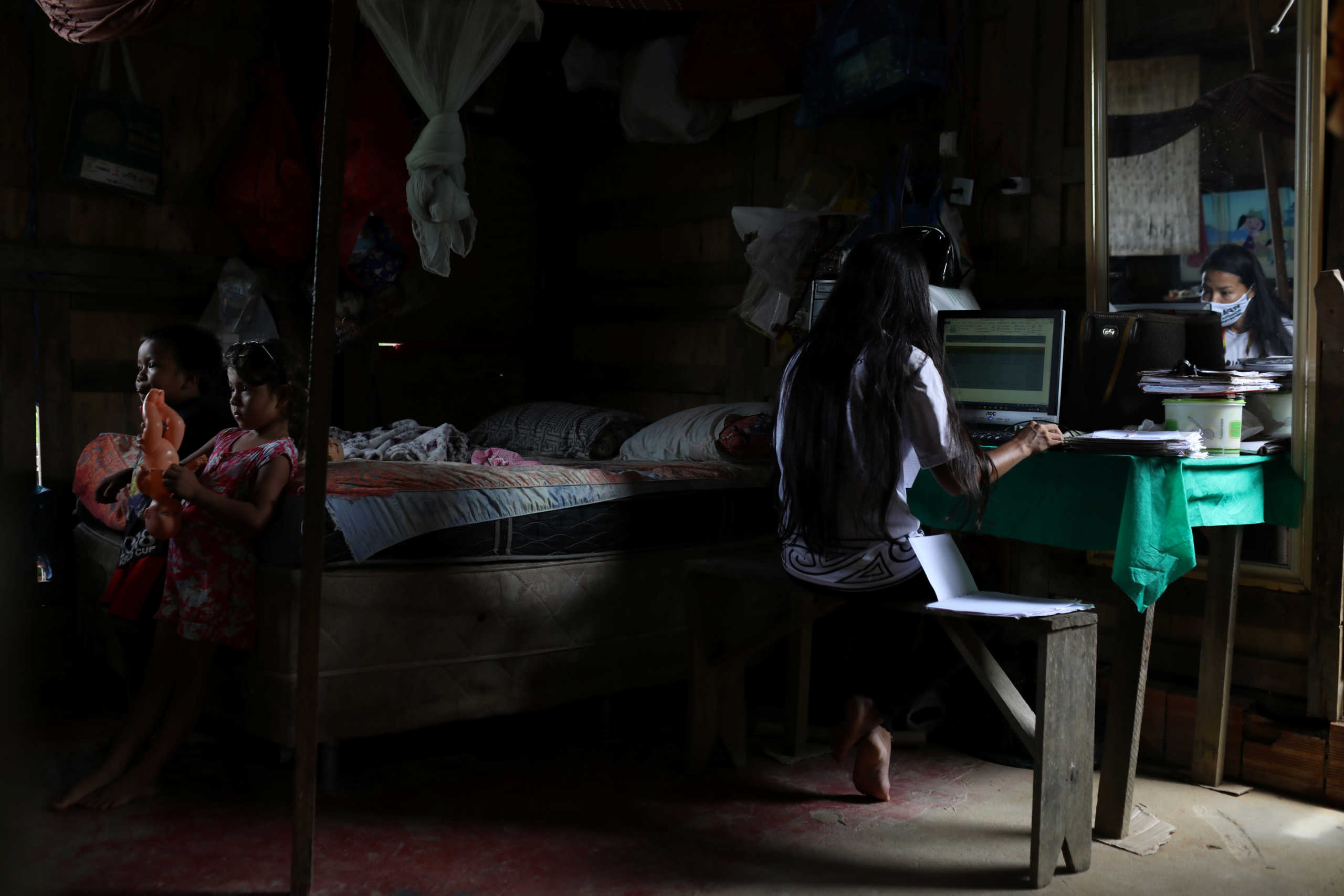 Vanderlecia Ortega dos Santos, 32, a nurse from the Witoto tribe, an indigenous ethnic group, who has volunteered to provide the only frontline care protecting her indigenous community of 700 families from the COVID-19 outbreak, works on her computer as her niece Maria Eduarda Ribeiro Ortega, 4, and nephew Davi Ortega Vasques, 4, watch TV in the same room, at Santos's home in Parque das Trios, during the coronavirus disease (COVID-19) outbreak, in the Taruma district, Manaus, Brazil, April 30, 2020. "Because we were so devoid of public assistance, I took the initiative to start a campaign on social media to receive donations of food and hygiene kits," said Santos. REUTERS