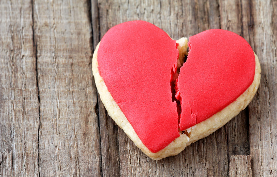 Cracked heart shaped cookie decorated with red icing as a concept of broken heart, breakup and end of relationship