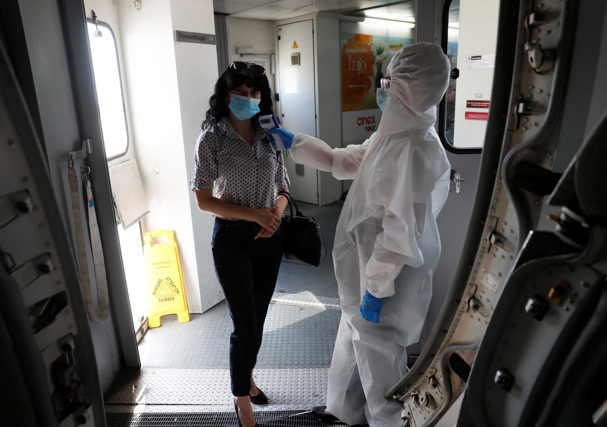 A stewardess wearing protective gear takes the body temperature of a woman at the entrance of a plane at the Boryspil International Airport outside Kiev, Ukraine June 13, 2020. The airport prepares to resume regular international and domestic flights as Ukraine eases restrictions aimed to contain the spread of the coronavirus disease (COVID-19). REUTERS