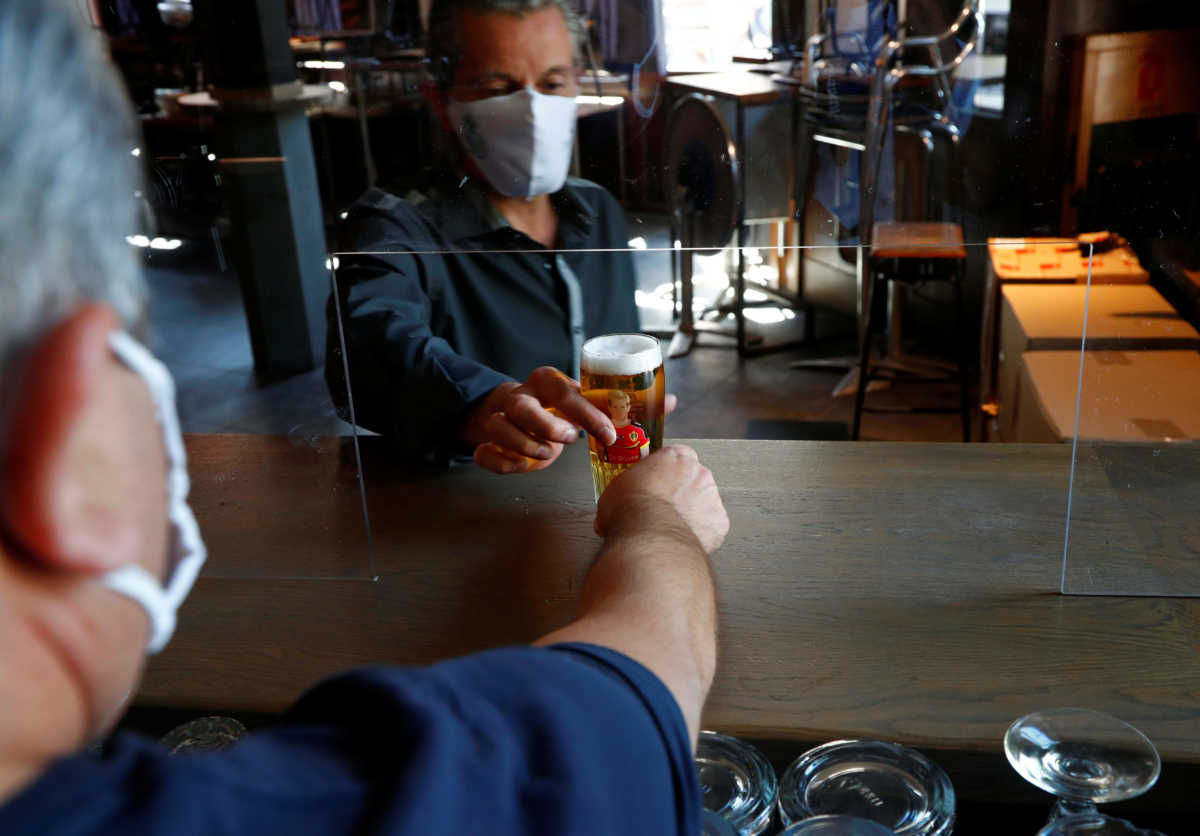 Romolo Putzu, owner of Le Louvre bar, gives a glass of beer to his waiter as he tests a protective plexiglass screen installed on the counter of his bar, as the country began easing lockdown restrictions amid the coronavirus disease (COVID-19) outbreak, in Brussels, Belgium, May 29, 2020. Picture taken May 29, 2020. REUTERS