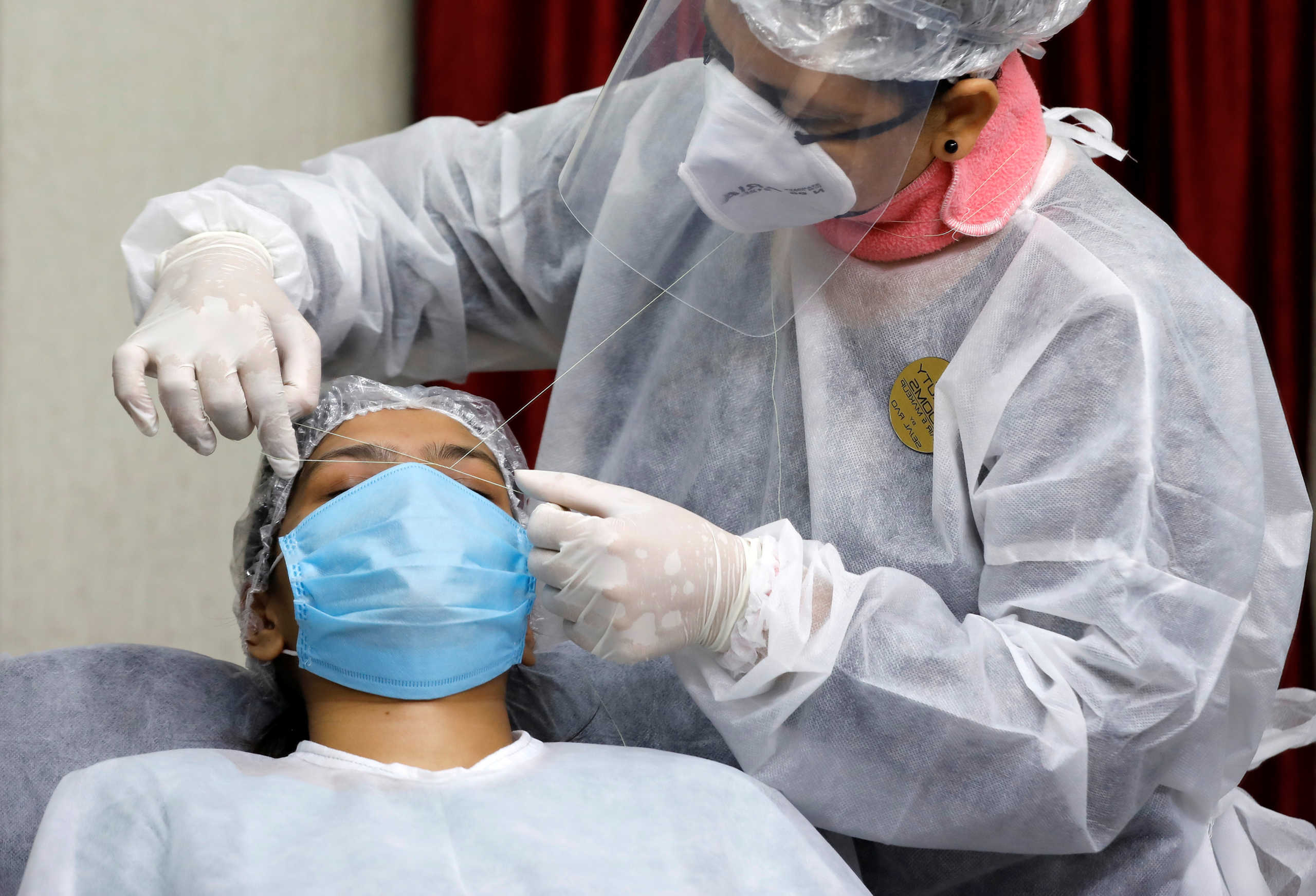 A woman gets her eyebrows threaded by a beautician wearing a protective gear inside a parlor after authorities allowed saloons and beauty parlors to open, during an extended nationwide lockdown to slow the spreading of the coronavirus disease (COVID-19), in Ahmedabad, India, May 19, 2020. REUTERS