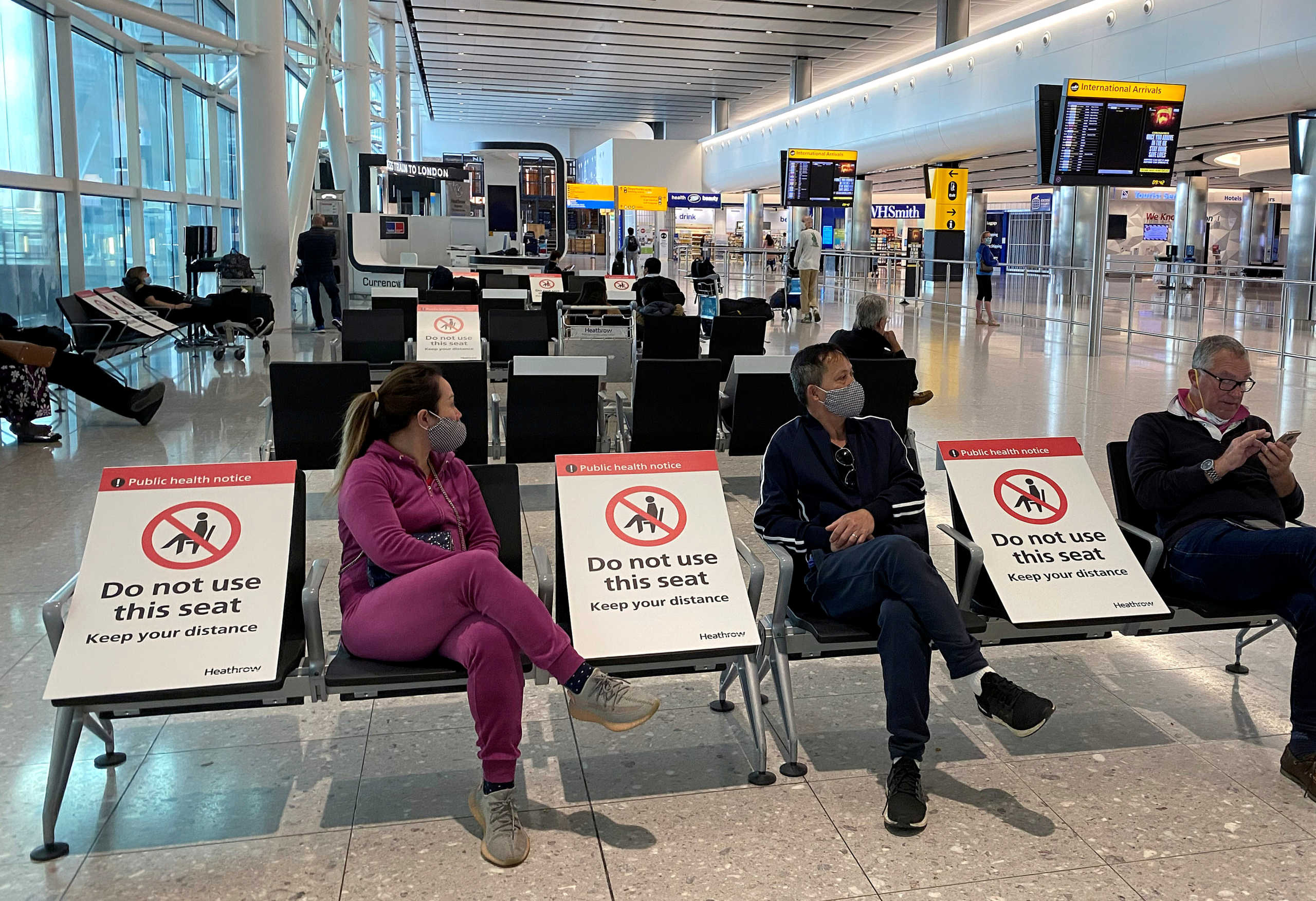 FILE PHOTO: People sit amongst socially-distanced seating signs at Heathrow Airport, as the spread of the coronavirus disease (COVID-19) continues, in London, Britain, May 10, 2020.  REUTERS