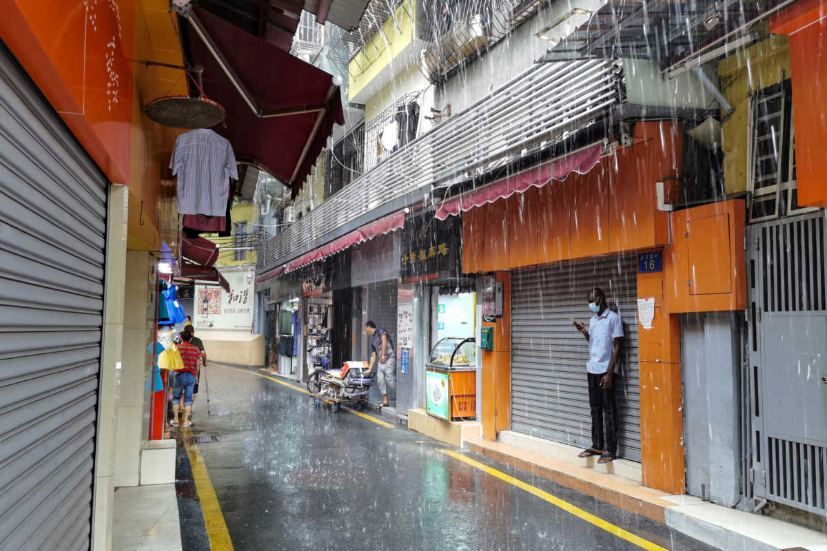 A man, wearing a face mask, shelters from the rain in Guangzhou's Xiaobei neighborhood, nicknamed "little Africa", as it starts to recover from a lockdown in April after the outbreak of the coronavirus disease (COVID-19), in Guangdong province, China June 17, 2020. Picture taken June 17, 2020. REUTERS