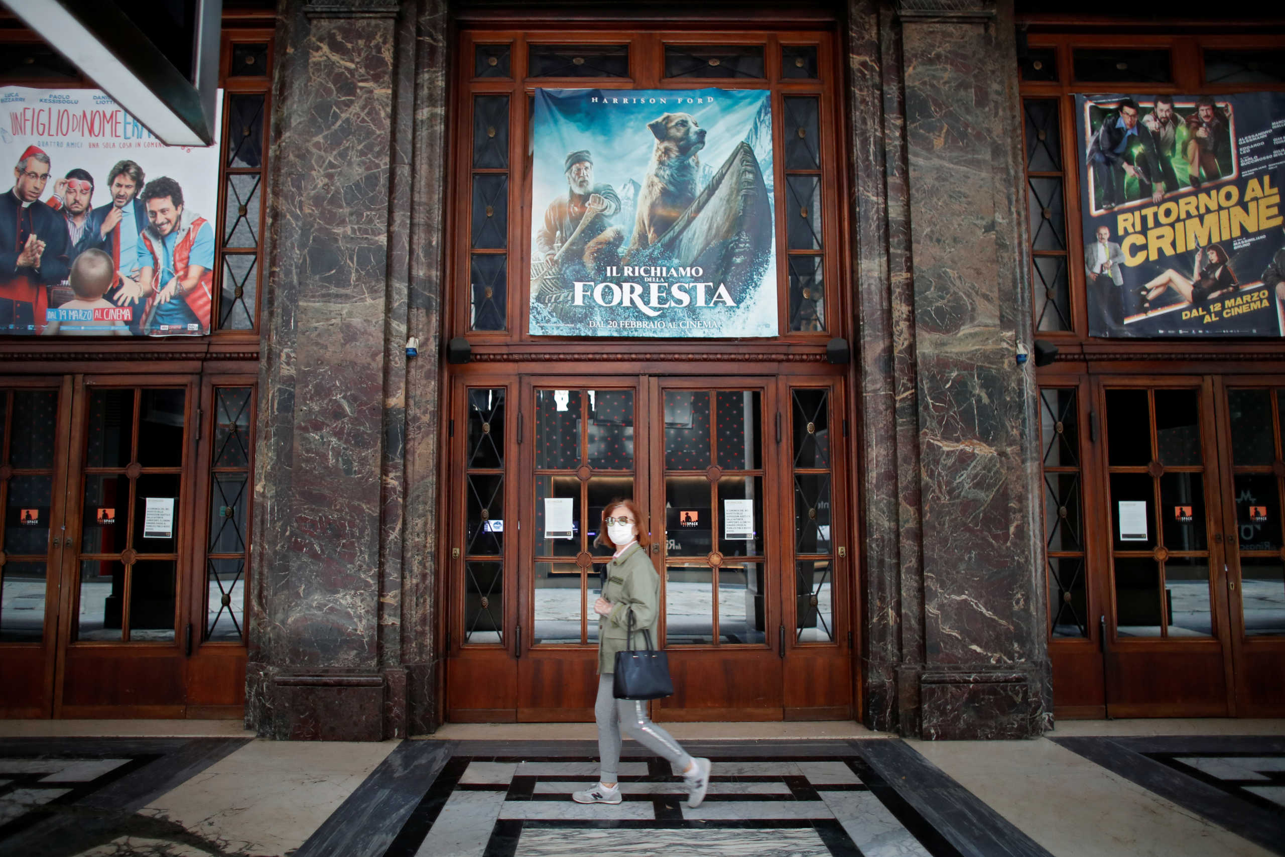 A woman wearing a face mask walks past movie posters as cinemas are closed due to the spread of the coronavirus disease (COVID-19) in Milan, Italy, May 16, 2020. REUTERS