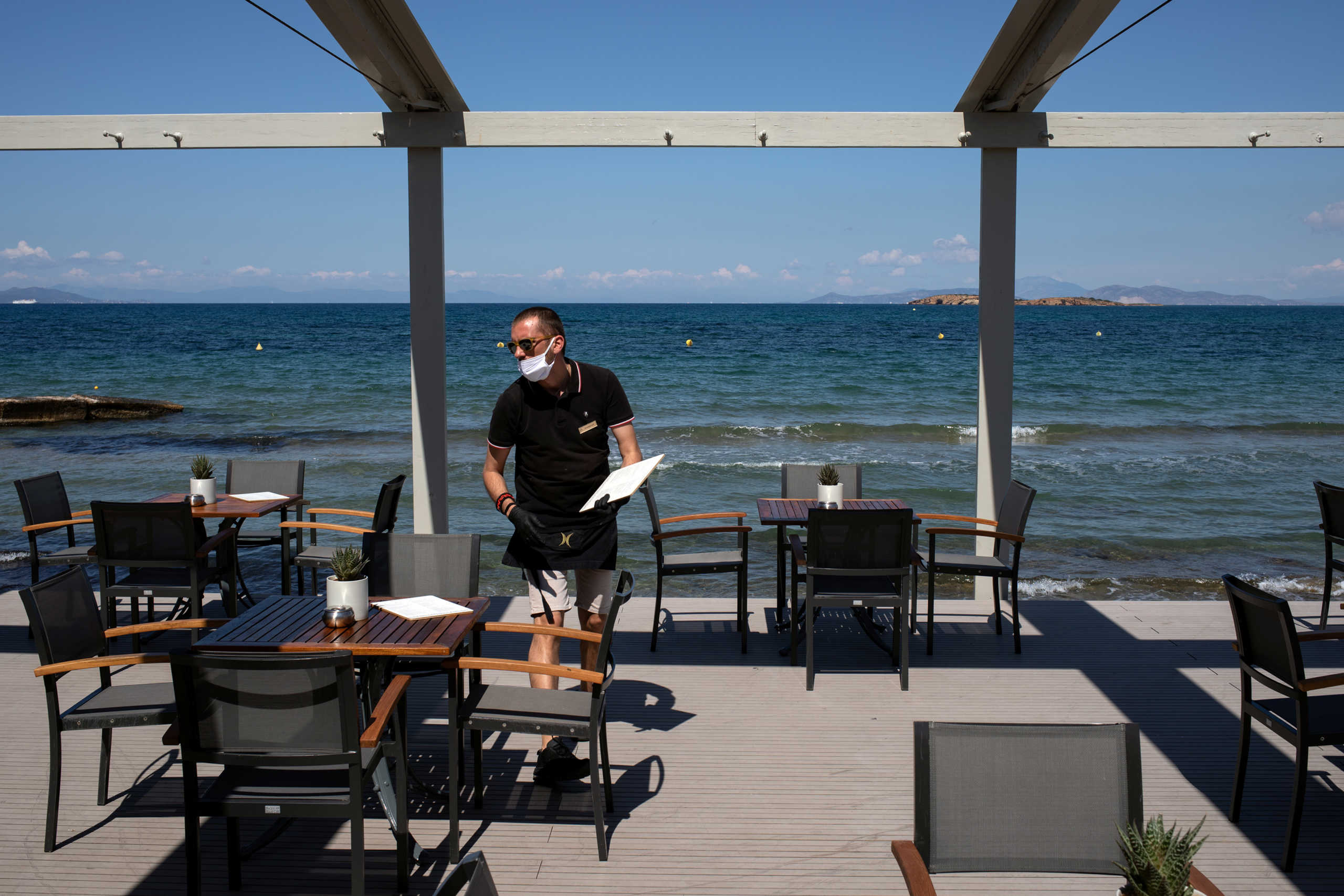 An employee wearing a protective mask, leaves a menu on a table at the beach bar of the Divani Apollon Palace hotel, on the first day of the opening of hotels in Greece, following a nationwide lockdown against the spread of the coronavirus disease (COVID-19), in Athens, Greece, June 1, 2020. REUTERS