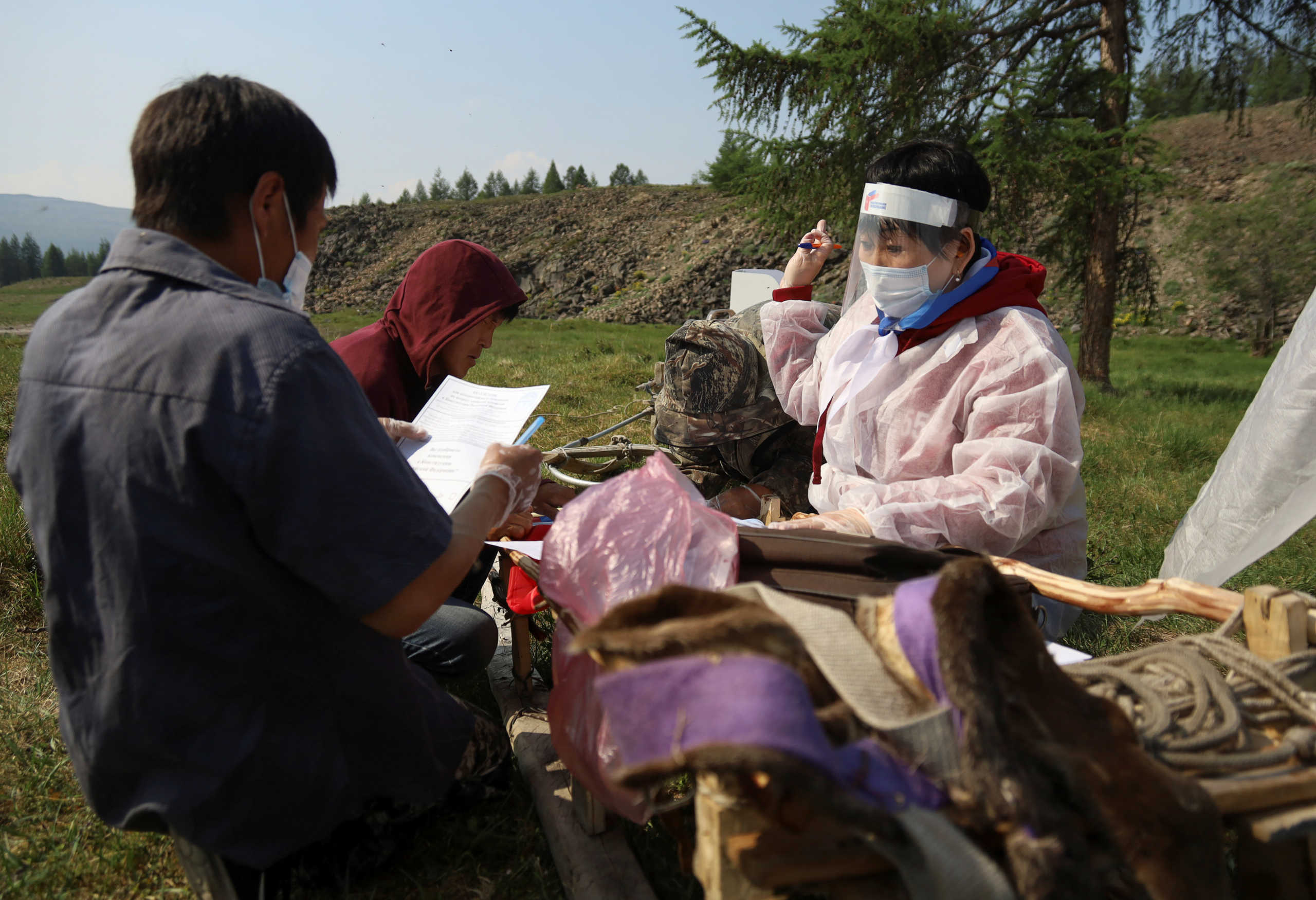 A member of an electoral commission wearing protective gear, used as a preventive measure against the spread of the coronavirus disease (COVID-19), hands over ballots to local residents during a seven-day nationwide vote on constitutional reforms in a remote settlement in the region of Yakutia in eastern Siberia, Russia June 25, 2020. Picture taken June 25, 2020. REUTERS