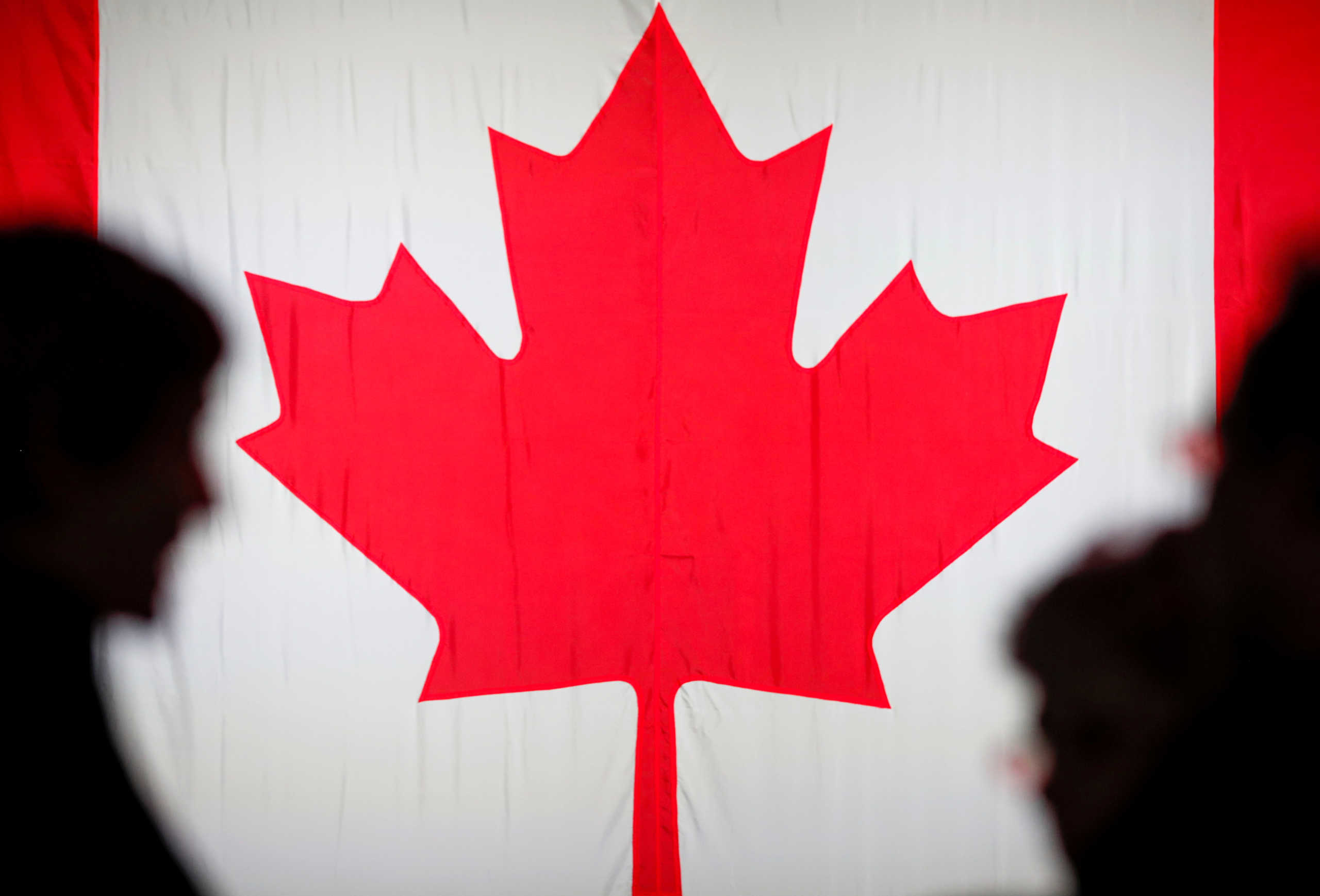FILE PHOTO: People are silhouetted in front of the Canadian national flag at the Palais des Congres in Montreal, Quebec, Canada October 21, 2019. REUTERS