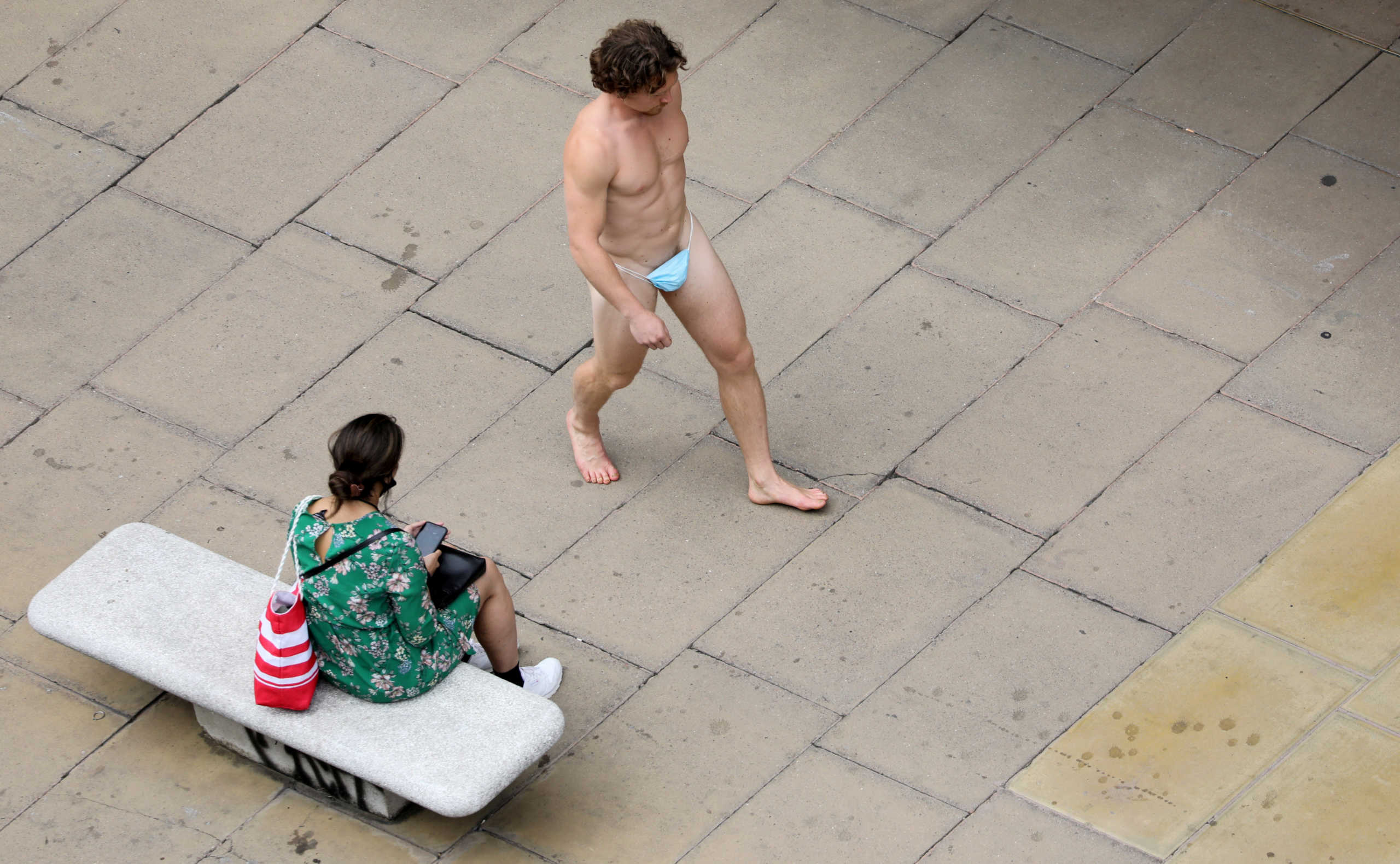 ATTENTION EDITORS - SENSITIVE MATERIAL. THIS IMAGE MAY OFFEND OR DISTURB A man wearing a surgical mask as G-string walks past a woman, as the spread of the coronavirus disease (COVID-19) continues, on Oxford Street in London, Britain July 24, 2020. REUTERS