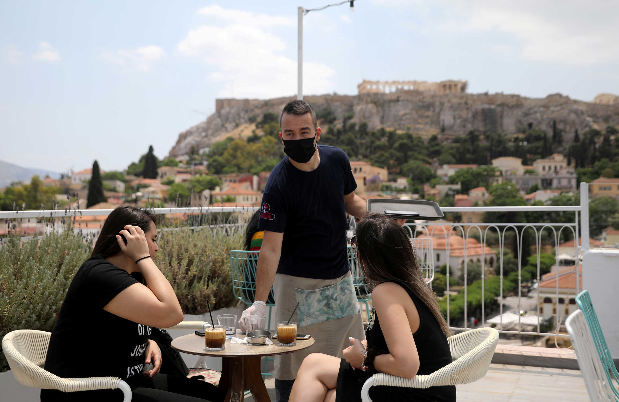 FILE PHOTO: A waiter wearing a protective face mask serves customers in a coffee shop, with the Acropolis hill in the background, as restaurants reopen following the easing of measures against the spread of the coronavirus disease (COVID-19), in Athens, Greece May 25, 2020. REUTERS