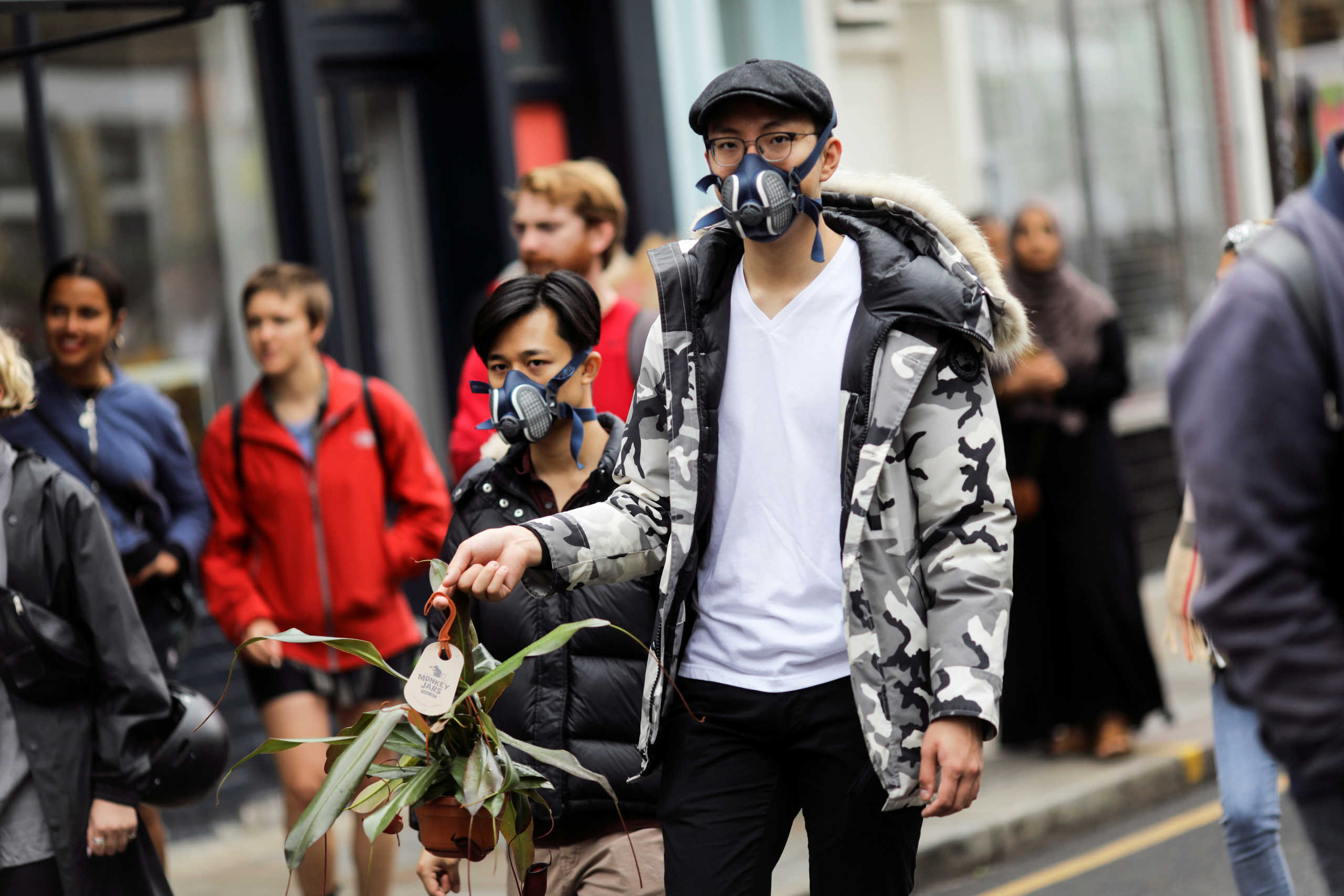 A man wearing a protective mask holds a plant as people walk down Columbia Road Flower Market after its reopening following the coronavirus disease (COVID-19) outbreak, in London, Britain, July 19, 2020. REUTERS