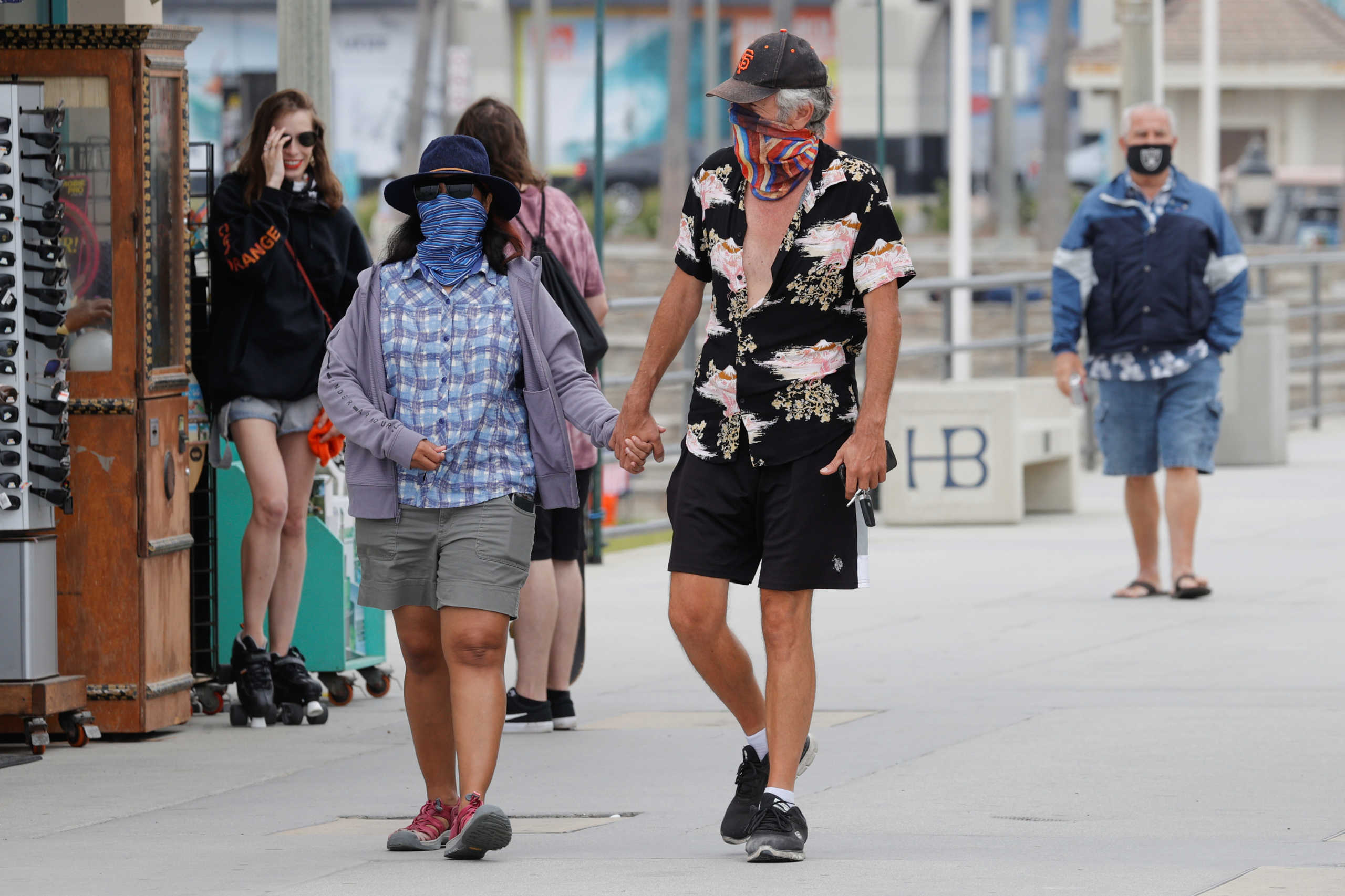 People wearing face masks walk along the ocean pier as the United States on Thursday passed a total of more than 4 million coronavirus infections during the global outbreak of the coronavirus disease (COVID-19) in Huntington Beach, California, U.S., July 23, 2020. REUTERS