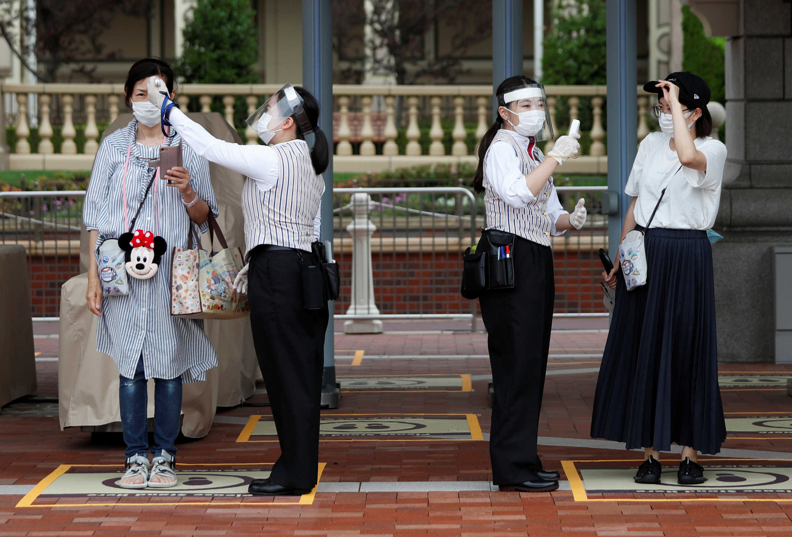 Tokyo Disneyland resort staff members conduct a body temperature check for visitors before the reopening of Tokyo Disneyland along with Tokyo DisneySea, which closed for months due to the coronavirus disease (COVID-19) outbreak, at the entrance gate of the Tokyo Disneyland in Urayasu, east of Tokyo, Japan July 1, 2020.  REUTERS