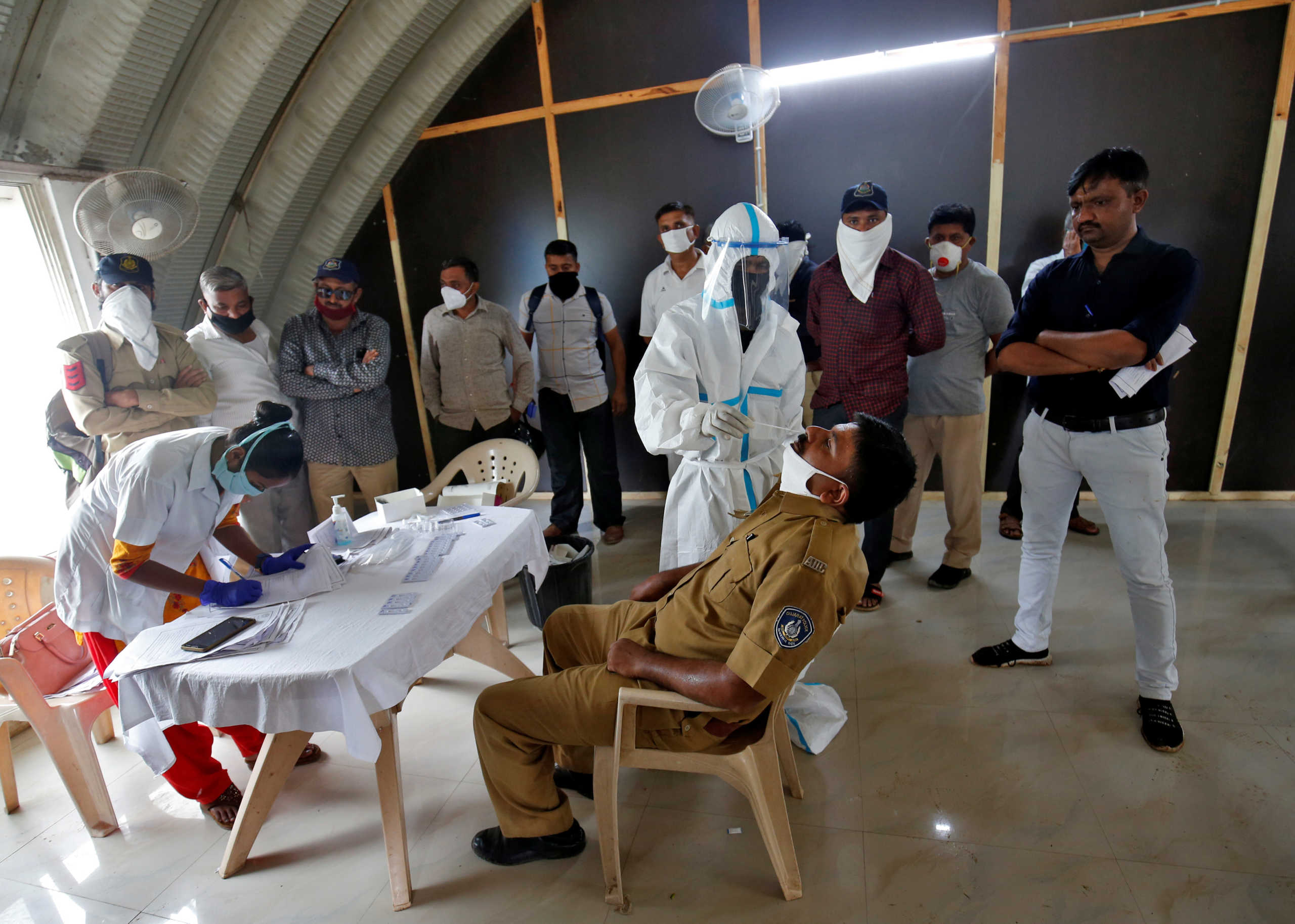 A healthcare worker wearing personal protective equipment (PPE) takes a swab from a police officer for a rapid antigen test inside a police headquarter, amidst the coronavirus disease (COVID-19) outbreak, in Ahmedabad, India, August 18, 2020. REUTERS