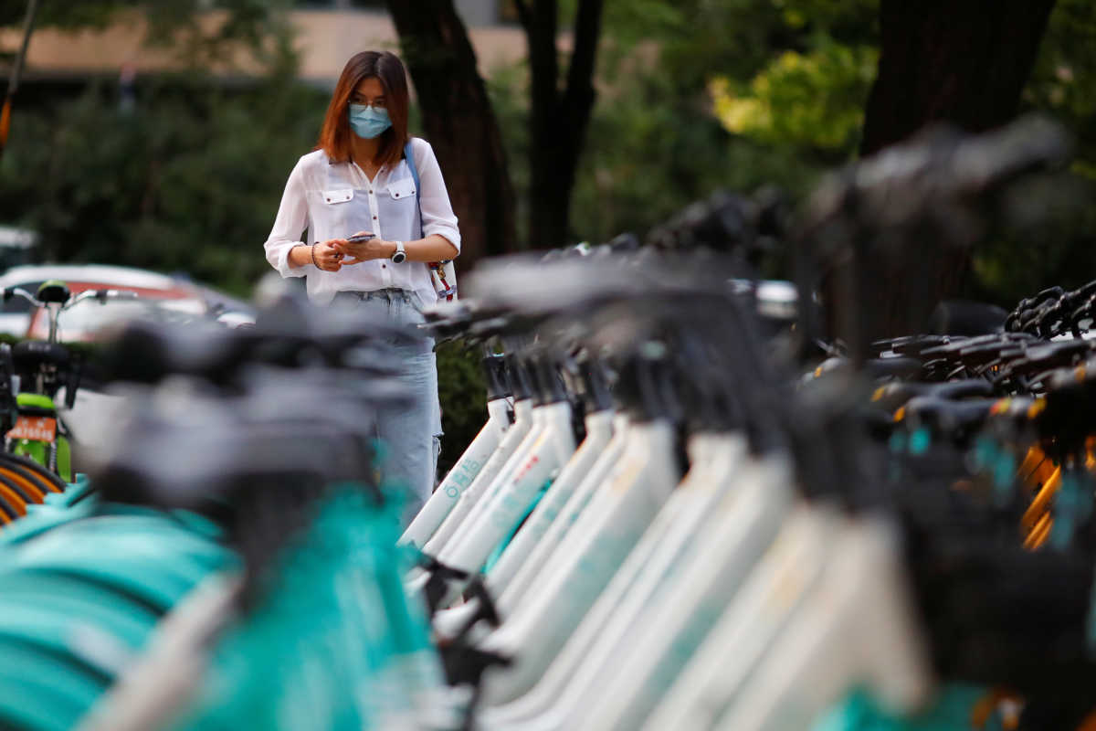 A woman uses her phone to unlock a Didi shared bicycle in the Central Business District following an outbreak of the coronavirus disease (COVID-19) in Beijing, China, August 4, 2020. Picture taken August 4, 2020.  REUTERS
