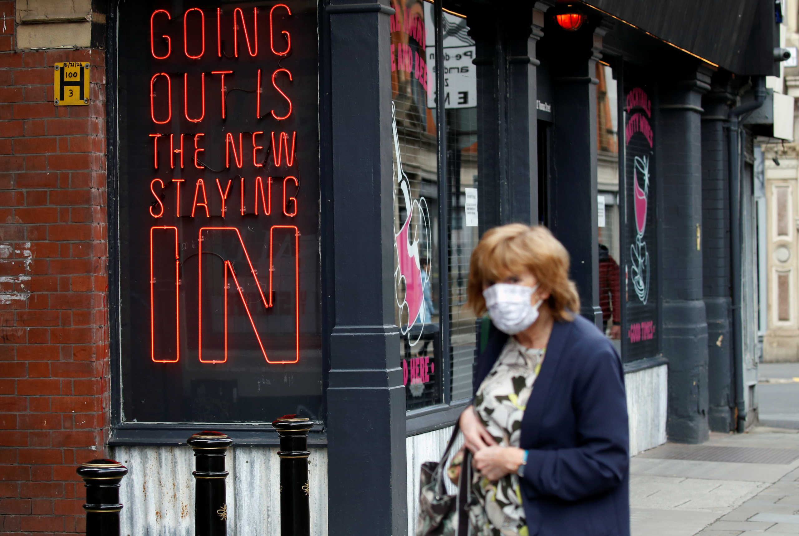 A woman wearing a protective face mask walks past a sign, as the city and surrounding areas face local restrictions in an effort to avoid a local lockdown being forced upon the region, amid the coronavirus disease (COVID-19) outbreak, in Manchester, Britain August 3, 2020. REUTERS