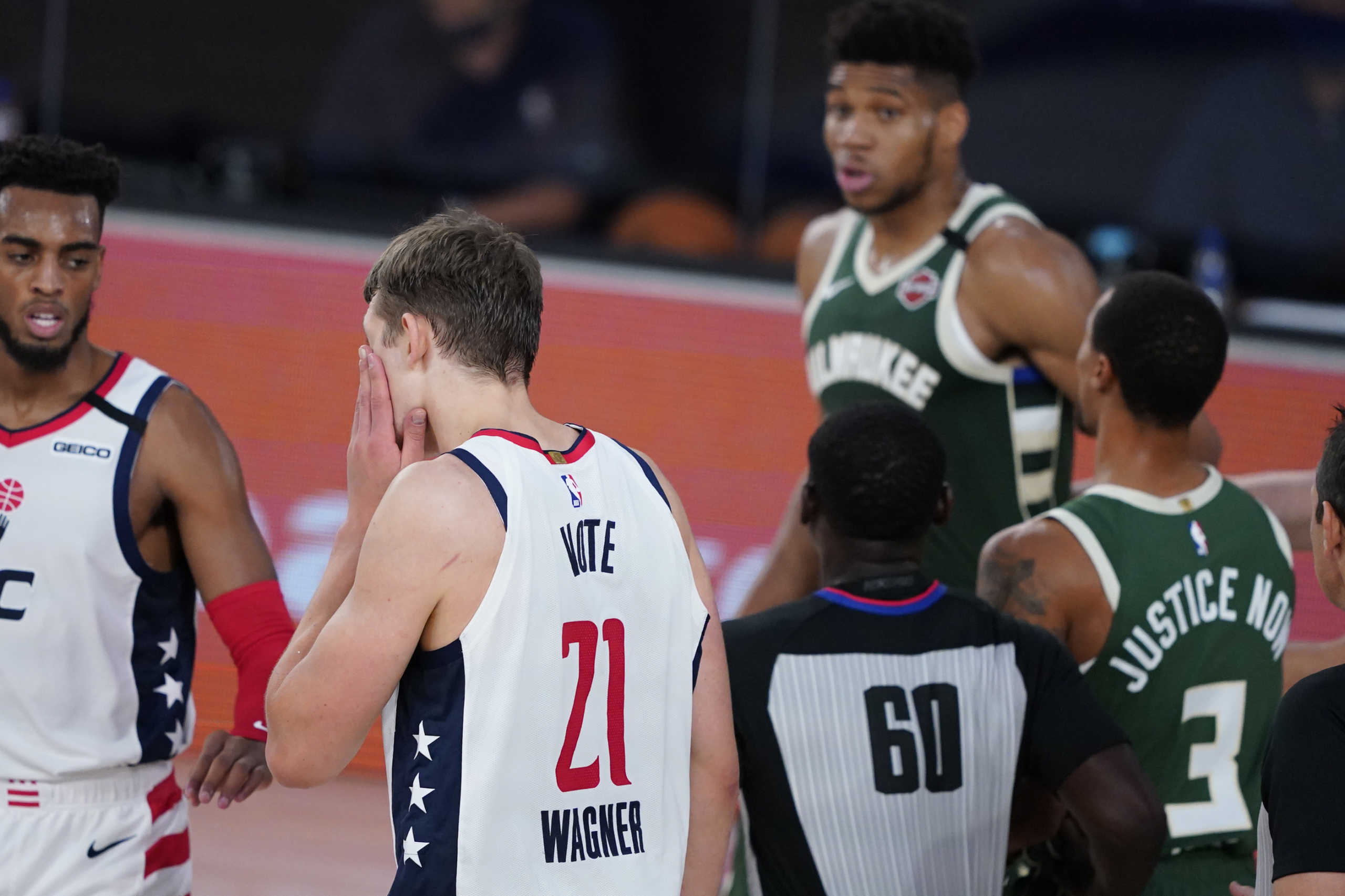 Aug 11, 2020; Lake Buena Vista, Florida, USA; Washington Wizards' Moritz Wagner (21) grabs his face after getting head butted by Milwaukee Bucks' Giannis Antetokounmpo, rear, during the first half of an NBA basketball game, Tuesday, Aug. 11, 2020, in Lake Buena Vista, Fla. at Visa Athletic Center.  Antetokounmpo was ejected from the game. Mandatory Credit: Ashley Landis