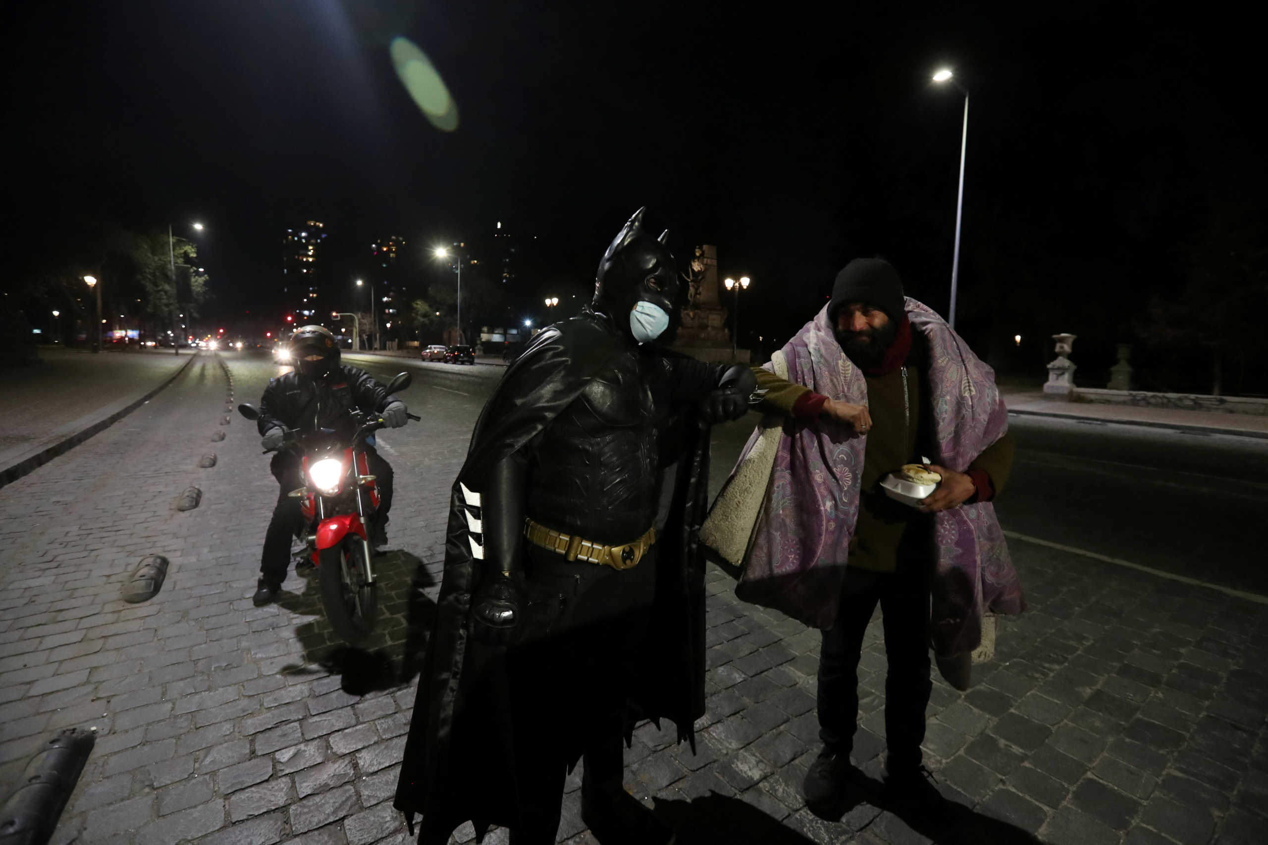 FILE PHOTO: A Chilean trader and so-called 'Batman solidario' (Solidarity Batman) greets a homeless man with an elbow bump while delivering charity food rations in the street, during the global outbreak of the coronavirus disease (COVID-19) in Santiago, Chile August 12, 2020. The man, who dresses up as the comic book superhero Batman, daily cooks around 100 food rations which he self-finances and distributes among neighbors and homeless people. 'Batman does not possess superpowers, he uses money and intelligence to help, he says.' Picture taken August 12, 2020. REUTERS