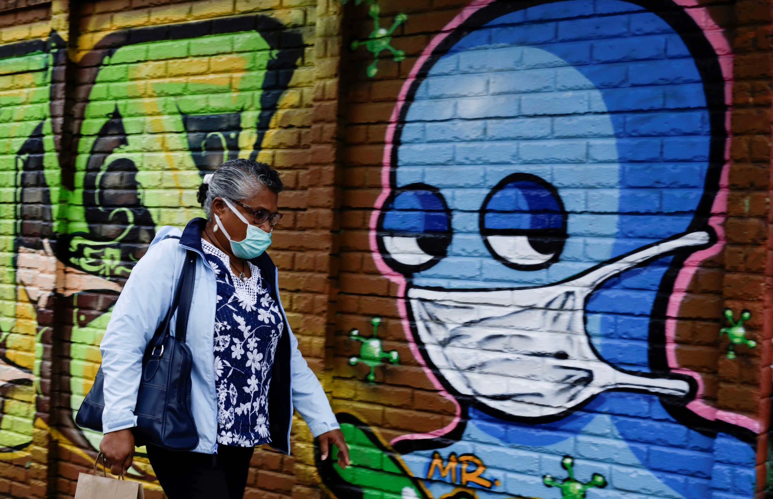FILE PHOTO: A woman wearing a protective face mask walks by a wall with graffiti after health authorities reverse the measures of reopening following the increase in cases of the coronavirus disease (COVID-19) in San Jose, Costa Rica July 13, 2020. REUTERS