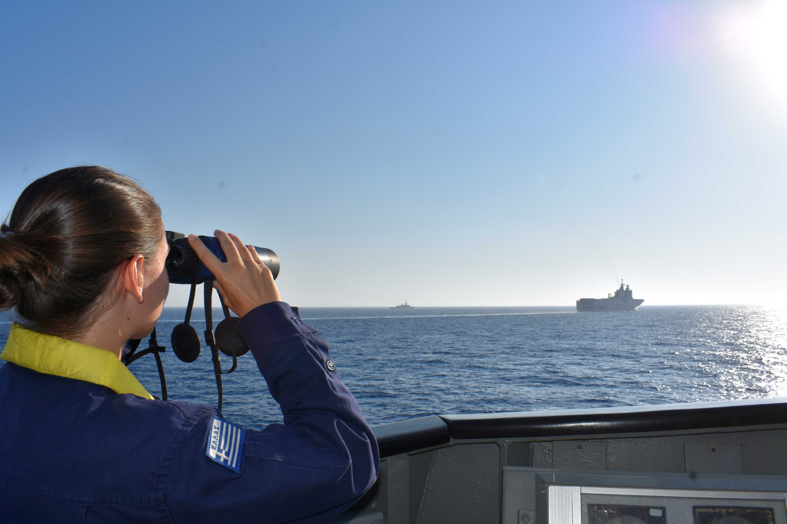 FILE PHOTO: A woman looks through binoculars as Greek and French vessels sail in formation during a joint military exercise in Mediterranean sea, in this undated handout image obtained by Reuters on August 13, 2020. Greek Ministry of Defence
