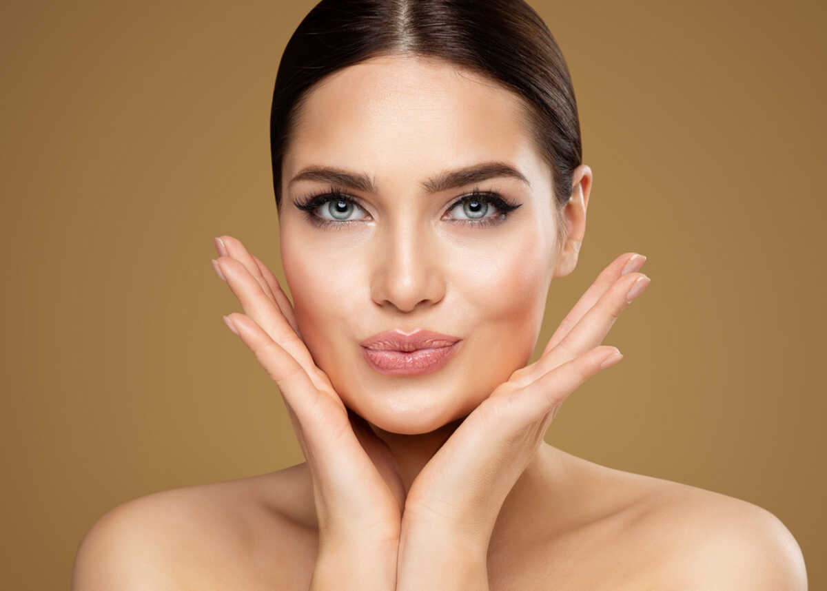 Beauty Model showing Cheekbones and Full Lips. Beautiful Woman Face Skin Care. Women Dermal Filler and Permanent Make up Cosmetology. Lip Augmentation Facial Lifting Spa Massage over Beige Background