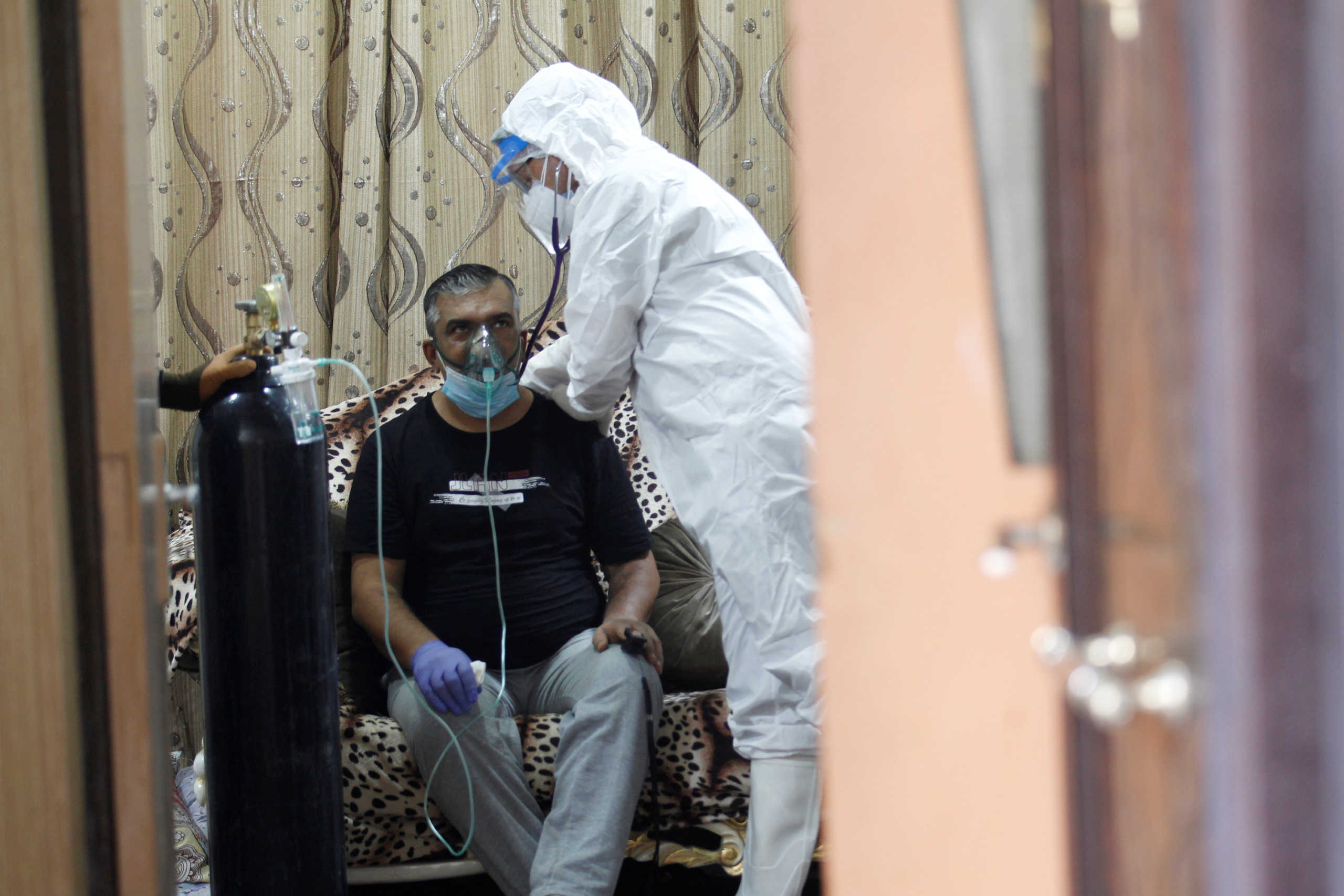 An Iraqi volunteer in a protective suit takes care of a patient infected with coronavirus disease (COVID-19), as he provides him with oxygen at home in the holy city of Najaf, Iraq, August 3, 2020. Picture taken August 3, 2020.  REUTERS