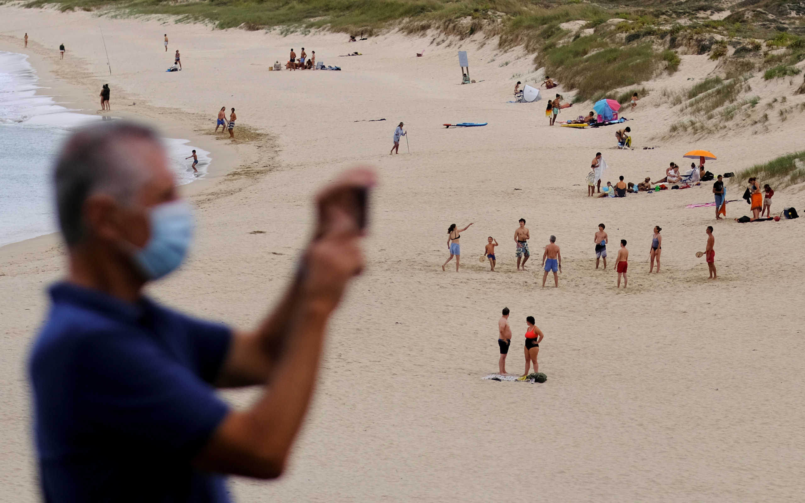 FILE PHOTO: A man wearing a face mask takes a picture as people enjoy sunny weather on San Xurxo beach on the coast of Ferrol, during the coronavirus disease (COVID-19) pandemic in the northwestern Spanish region of Galicia, Spain August 18, 2020. REUTERS