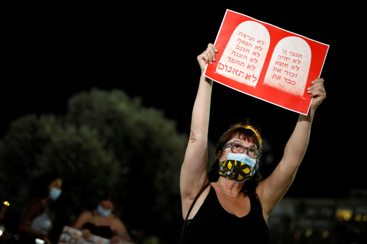 A woman holds a placard with the The Ten Commandments and an additional one in Hebrew reading "Do Not Rape" during a protest against sexual violence in Tel Aviv, Israel August 23, 2020. REUTERS