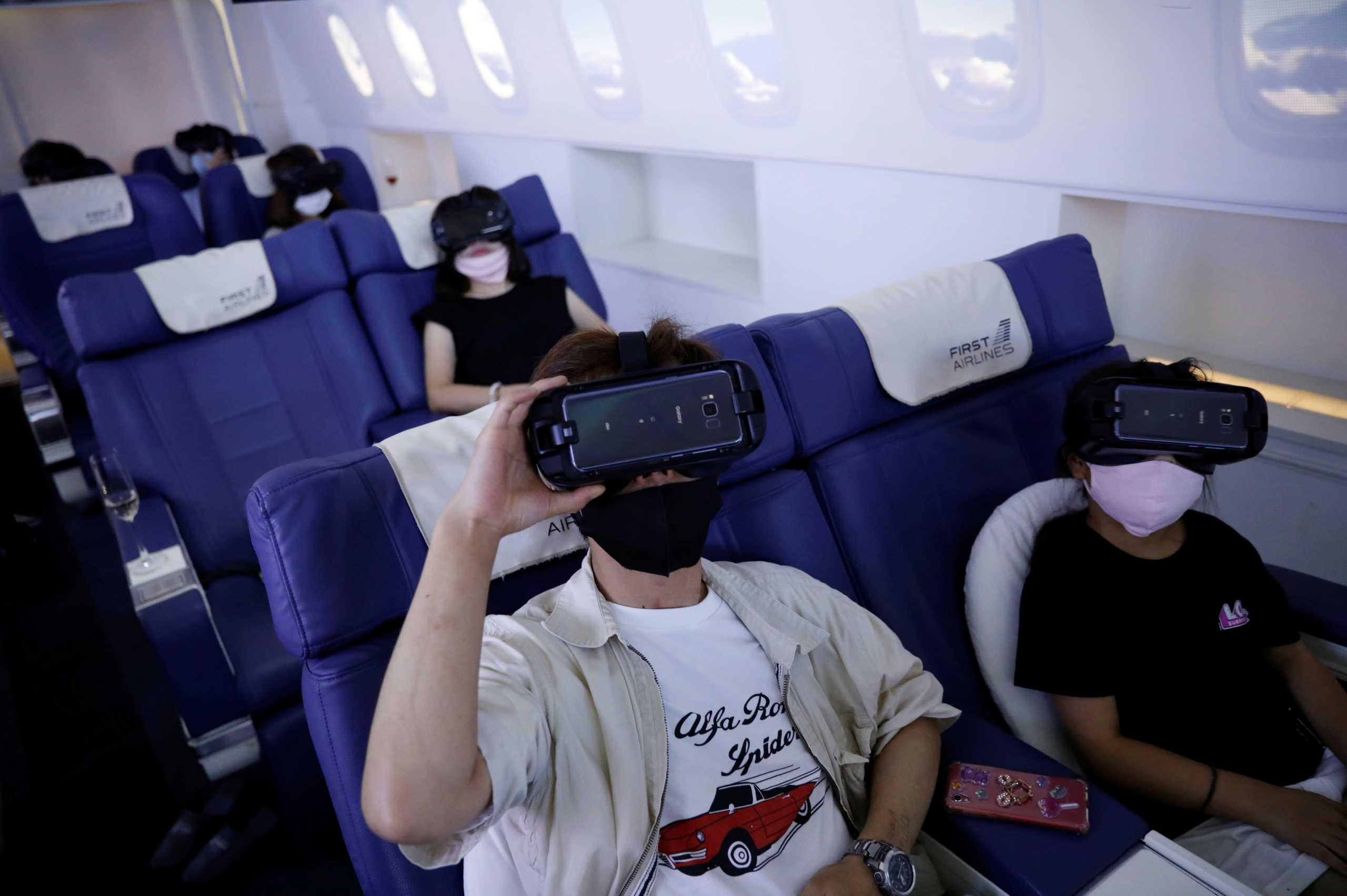Customers in flight seats use virtual reality (VR) devices at First Airlines, that provides VR flight experiences, including 360-degree tours of cities and meals, amid the COVID-19 pandemic in Tokyo, Japan August 12, 2020. REUTERS