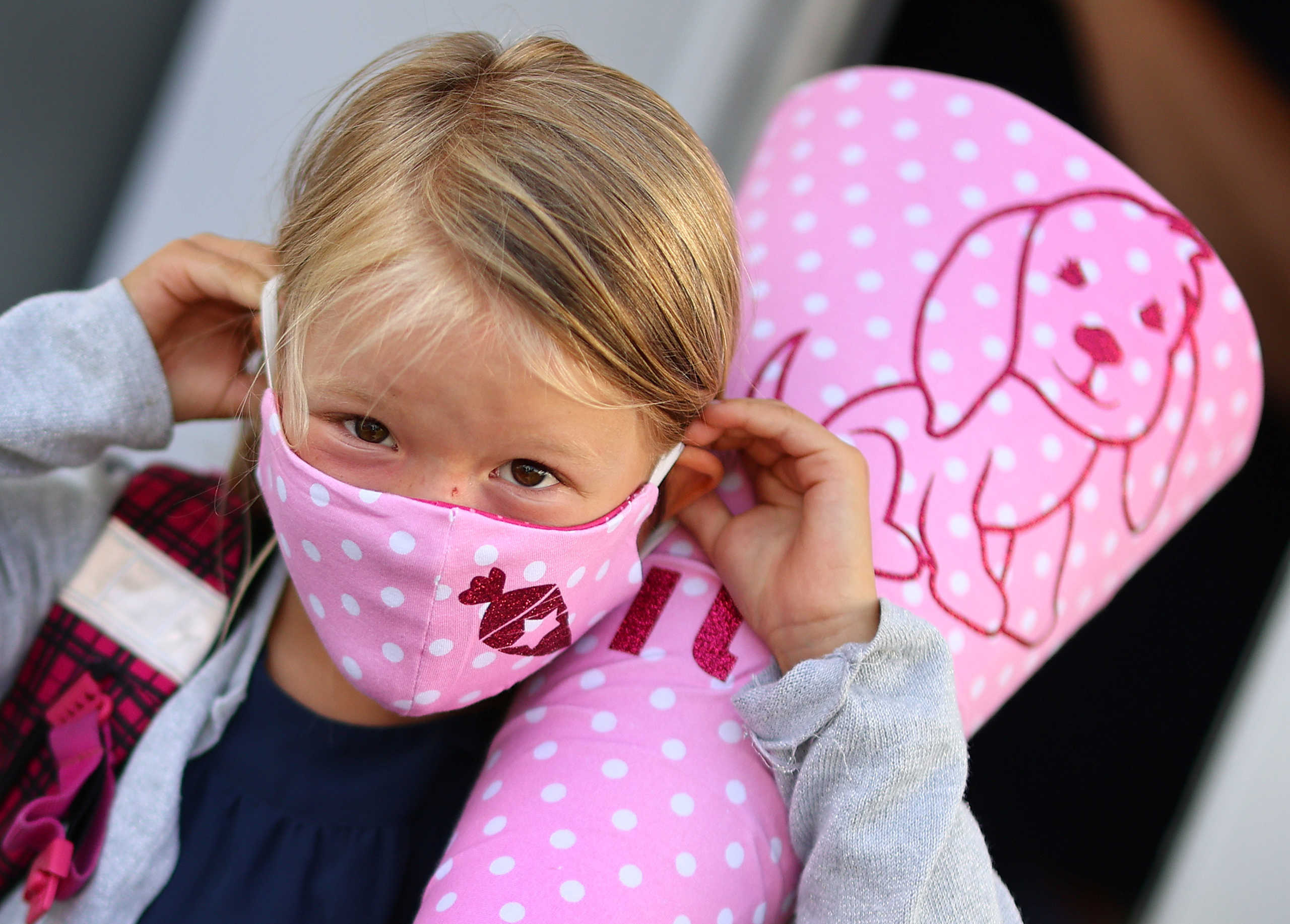 Six-year old Tilda adjusts her customised face mask before she walks to primary school for the first time after the lockdown due the outbreak of the coronavirus disease (COVID-19) in Rodenbach, Germany, August 18, 2020. REUTERS