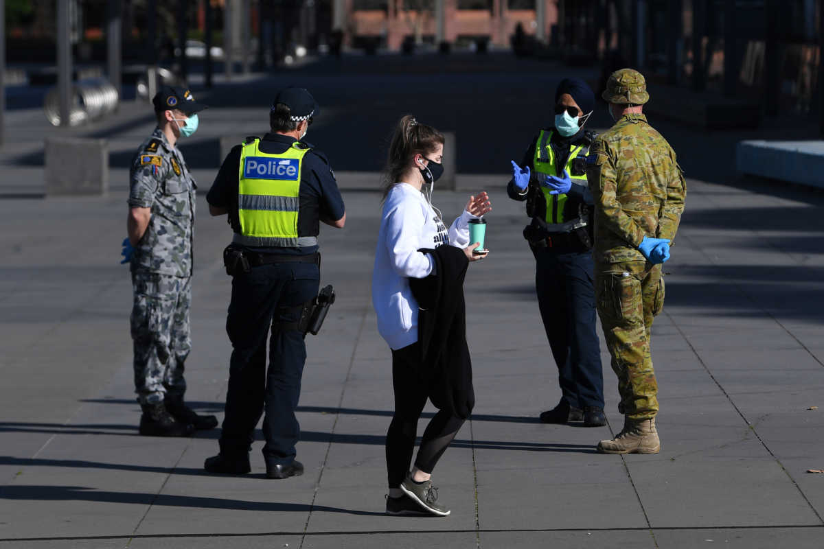 A person wearing a face mask walks past Victoria Police, Airforce and ADF personnel outside of the Melbourne Museum as the city operates under lockdown in response to an outbreak of the coronavirus disease (COVID-19) in Melbourne, Australia, August 21, 2020.  AAP Image
