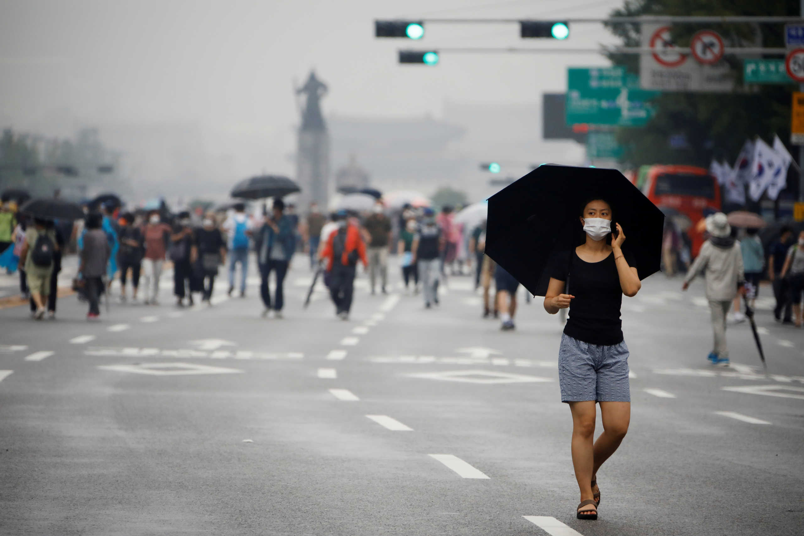 A woman wearing a mask walks past members of conservative civic groups who take part in an anti-government protest, as concerns over a fresh wave of the coronavirus disease (COVID-19) cases grow, in central Seoul, South Korea, August 15, 2020.    REUTERS
