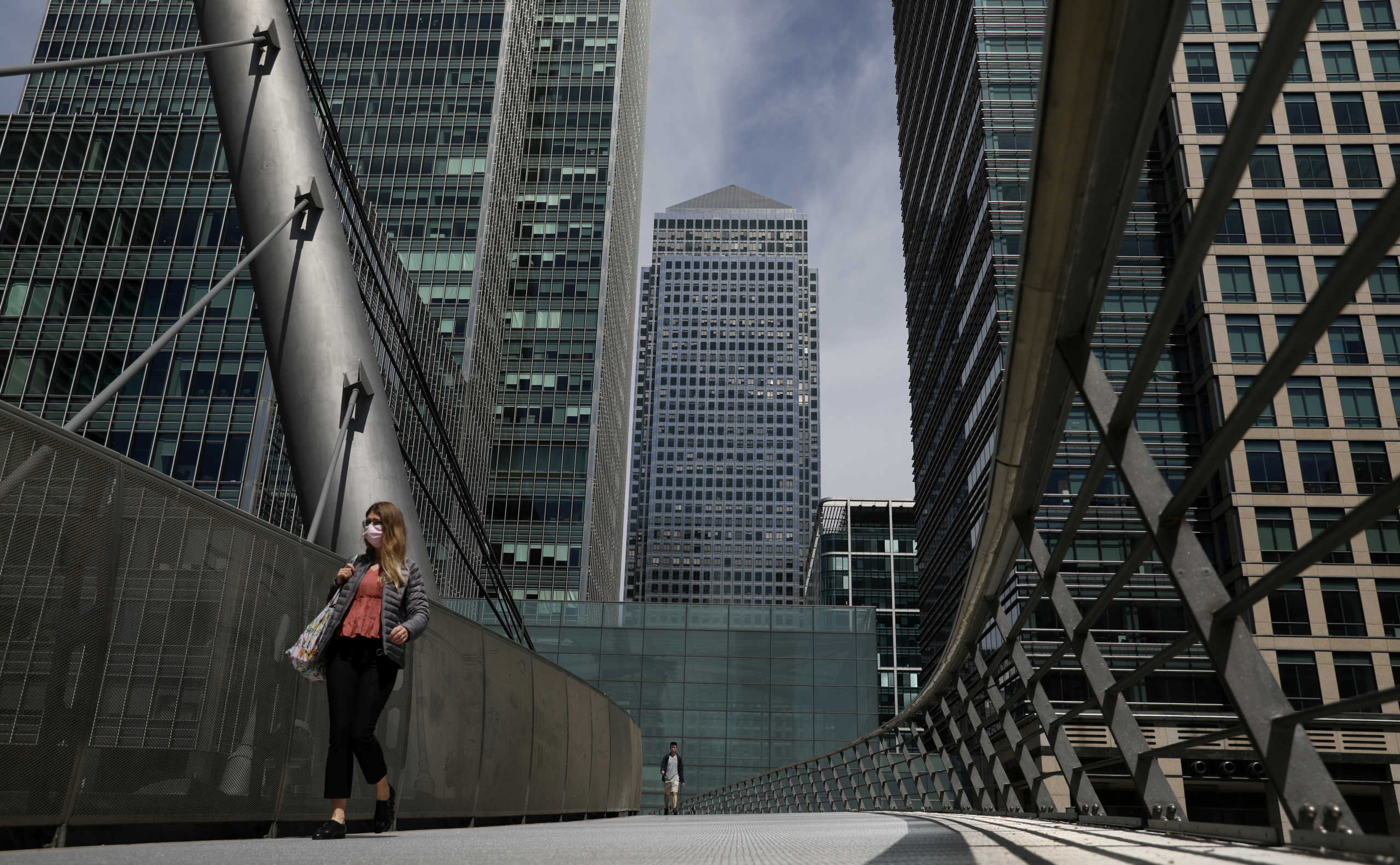 FILE PHOTO: A woman wearing a face mask crosses a bridge in front of One Canada Square in Canary Wharf, following the outbreak of the coronavirus disease (COVID-19), London, Britain, May 18, 2020. REUTERS