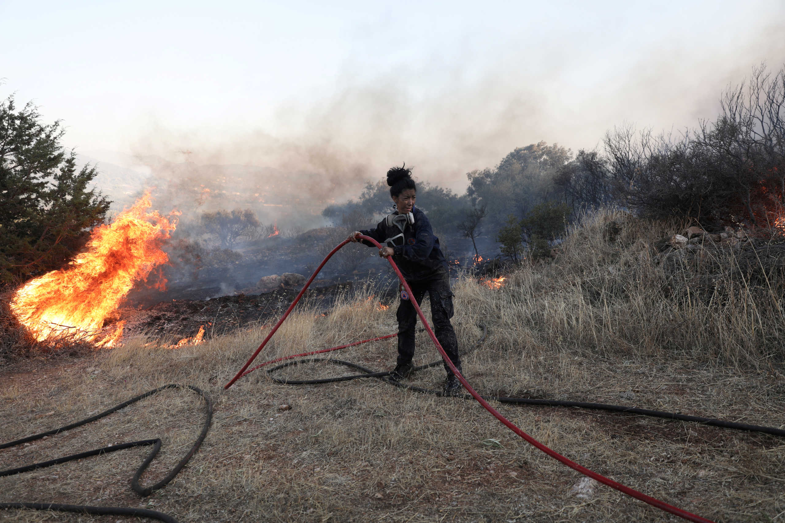 A firefighter holds a hose as a wildfire burns near the village of Anavissos, Greece, September 9, 2020. REUTERS